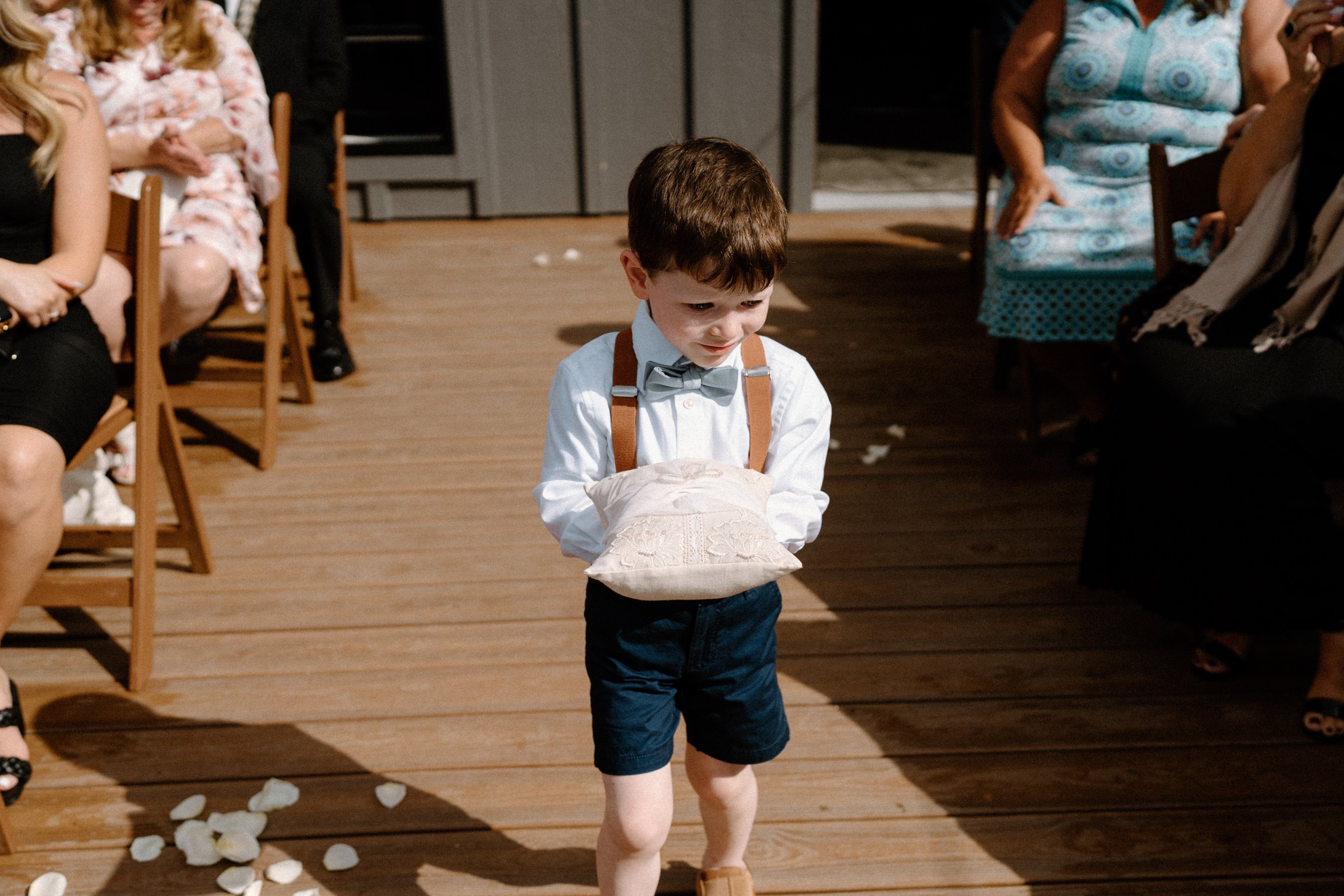 A young ring bearer walks down the aisle holding a pillow with the rings