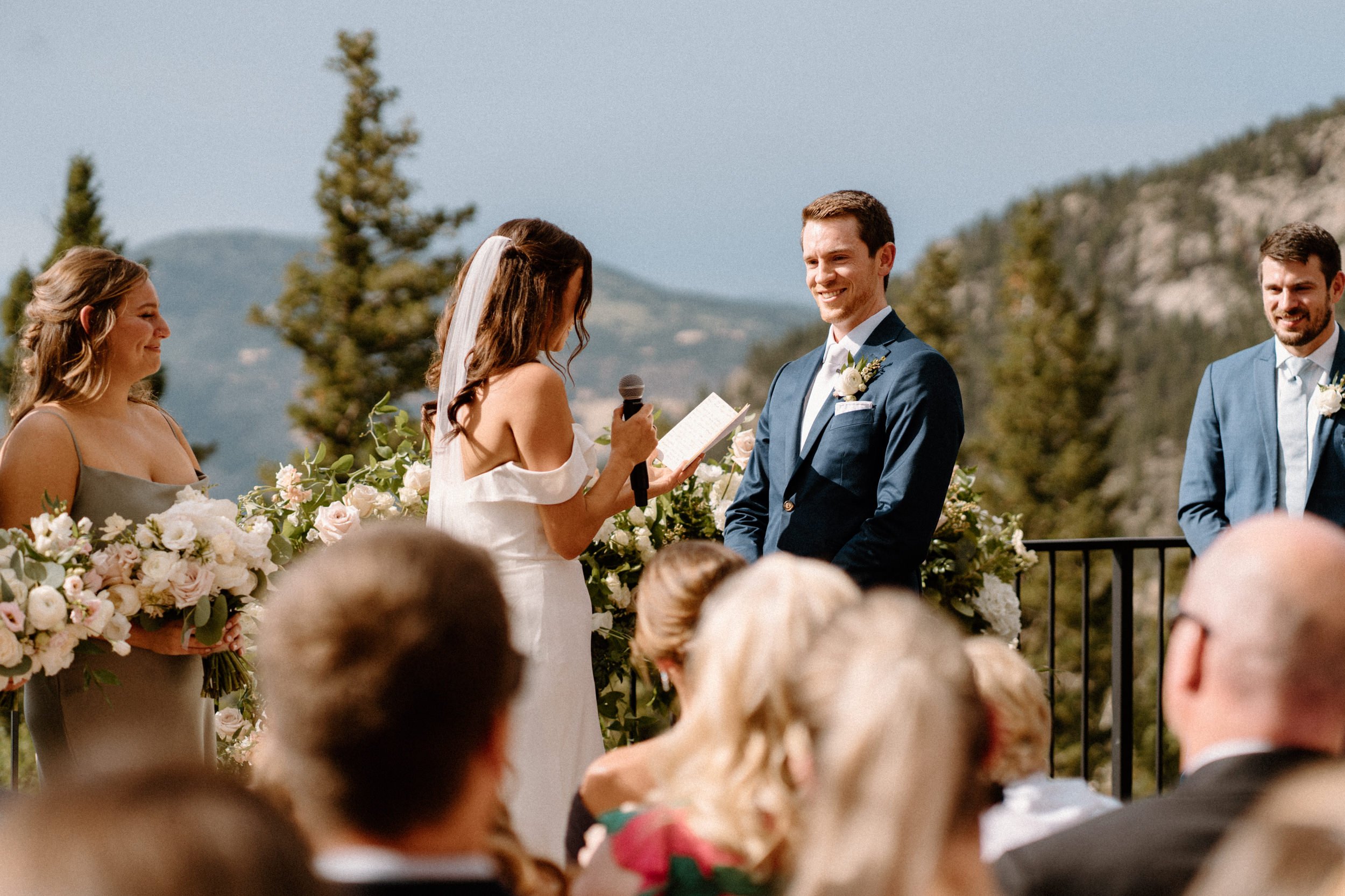 The groom smiles as the bride reads her vows aloud