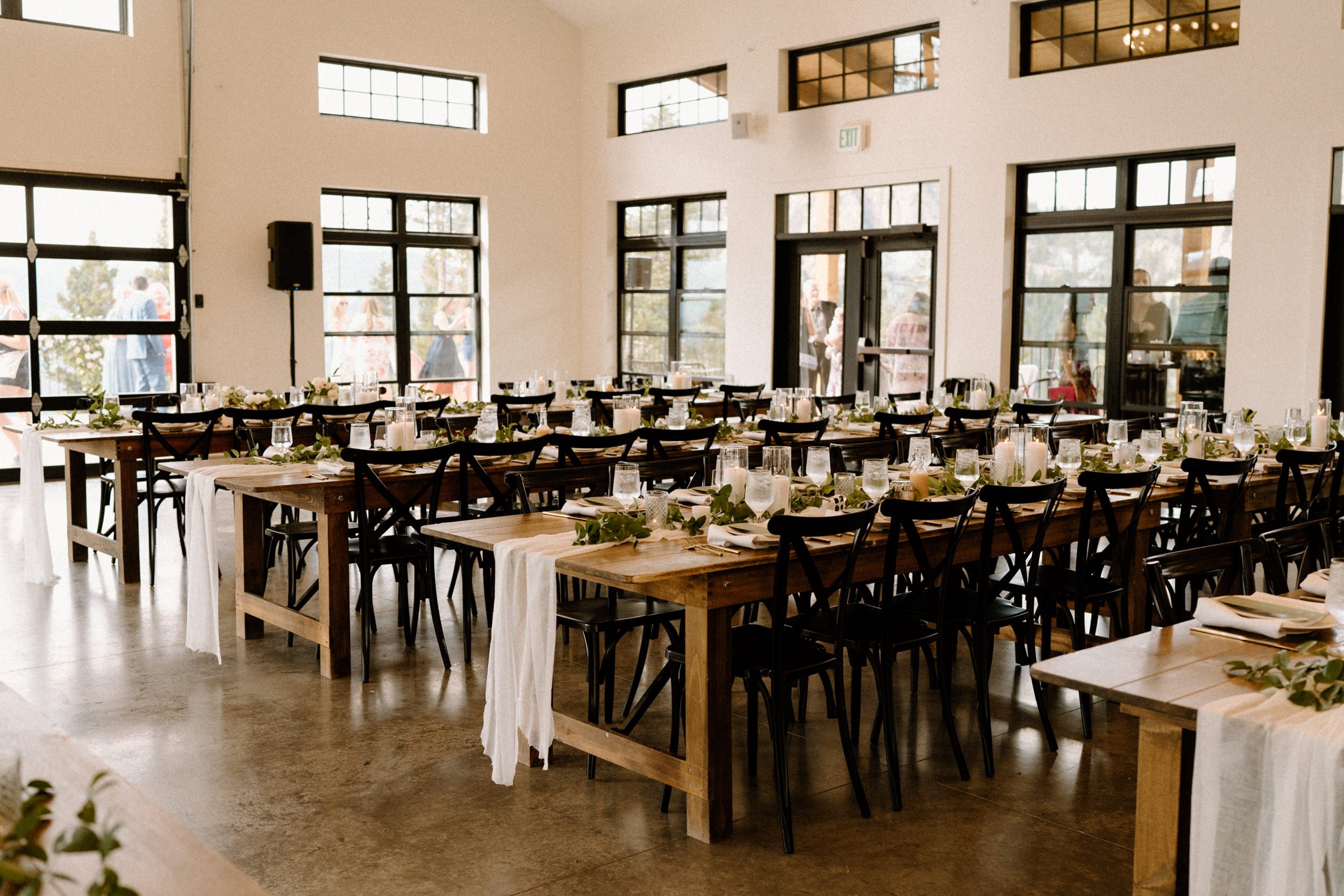 Wooden reception tables decorated with white cloth and greenery at North Star Gatherings in Idaho Springs, CO