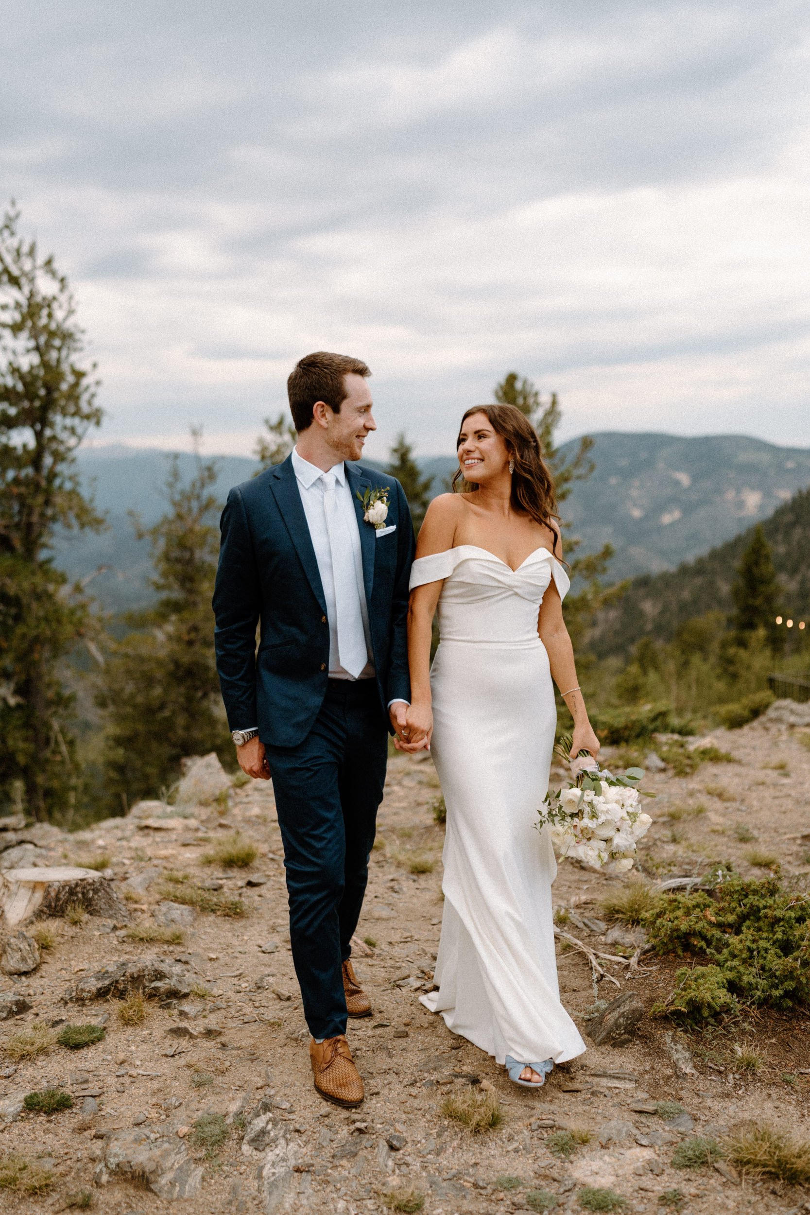 The bride and groom hold hands on a mountain overlook at North Star Gatherings in Idaho Springs, CO