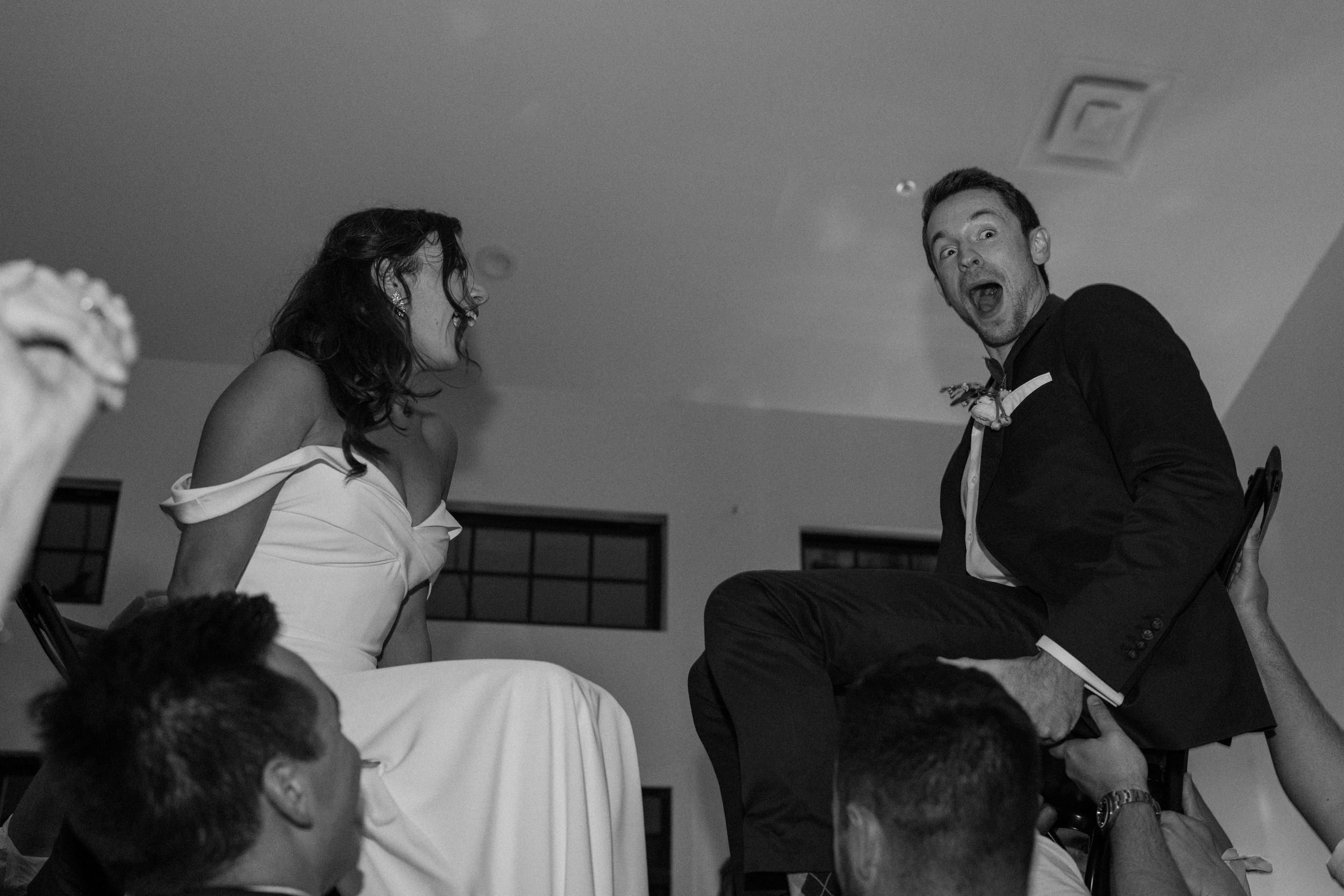 The bride and groom laugh as they are both lifted into the air