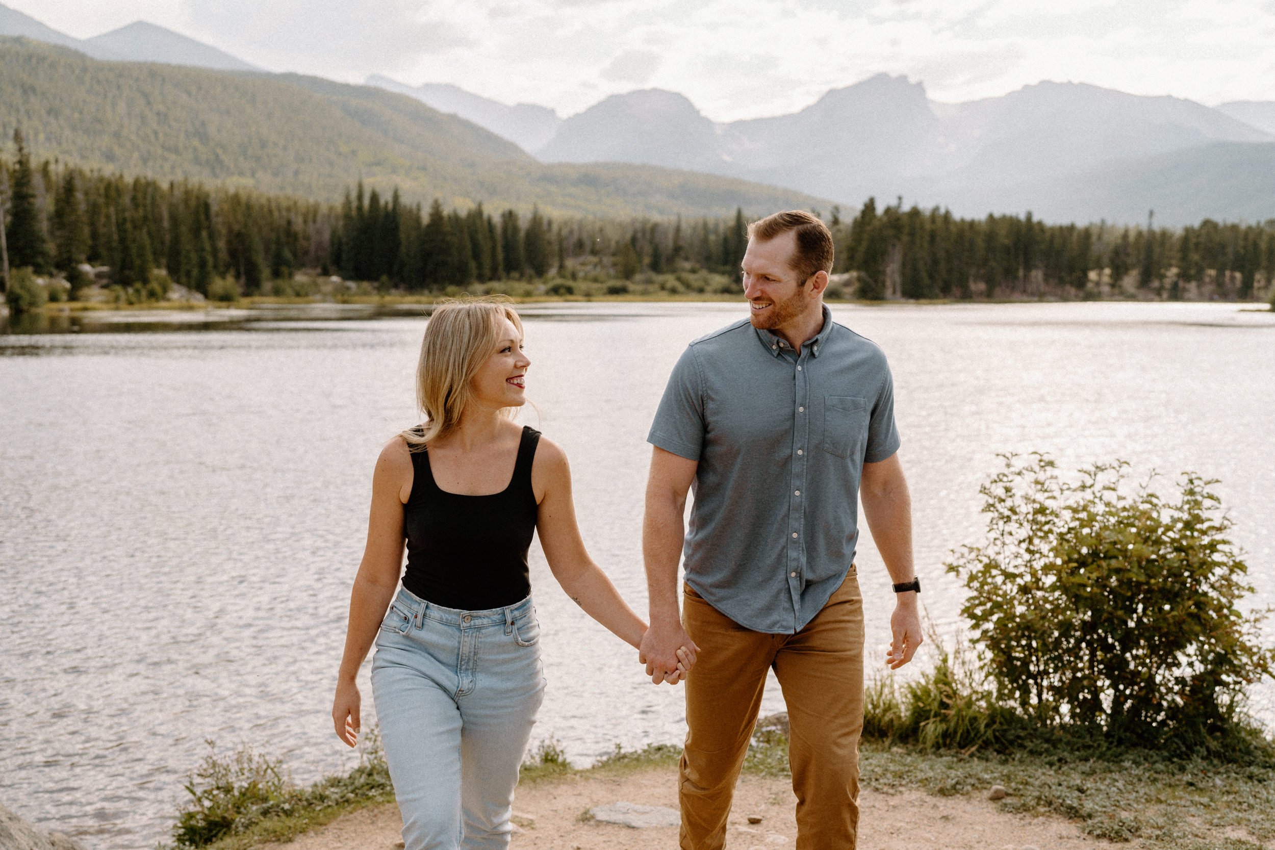 Man and woman hold hands walking on the shore of Sprague Lake at Rocky Mountain National Park