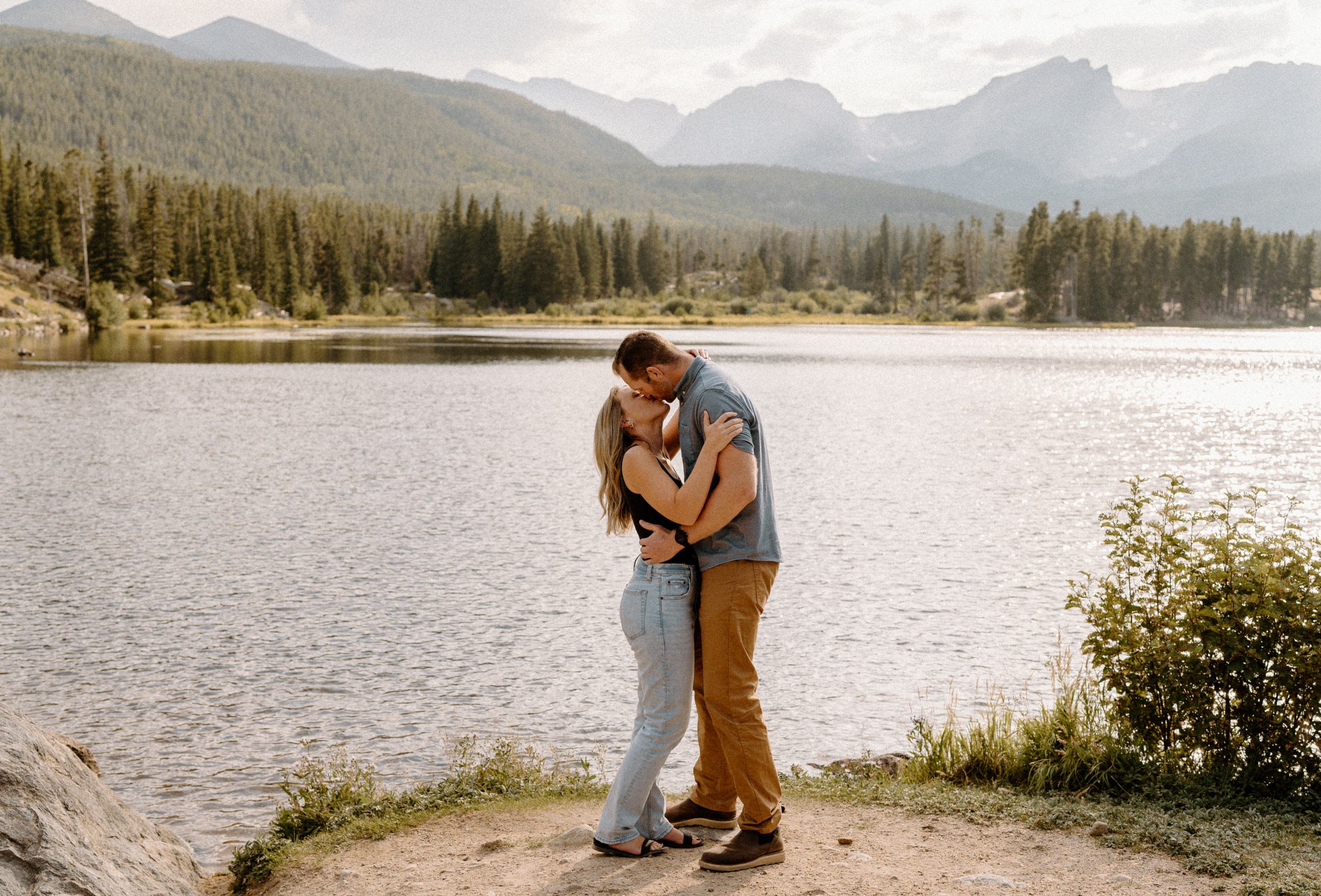 Man and woman kiss at Sprague Lake at Rocky Mountain National Park during engagement session