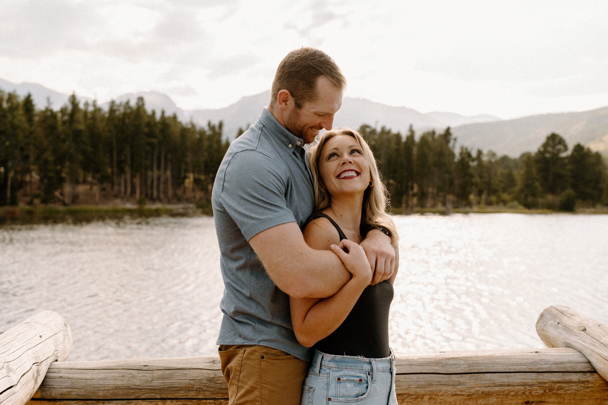 Woman smiles up to man as he hugs her from behind