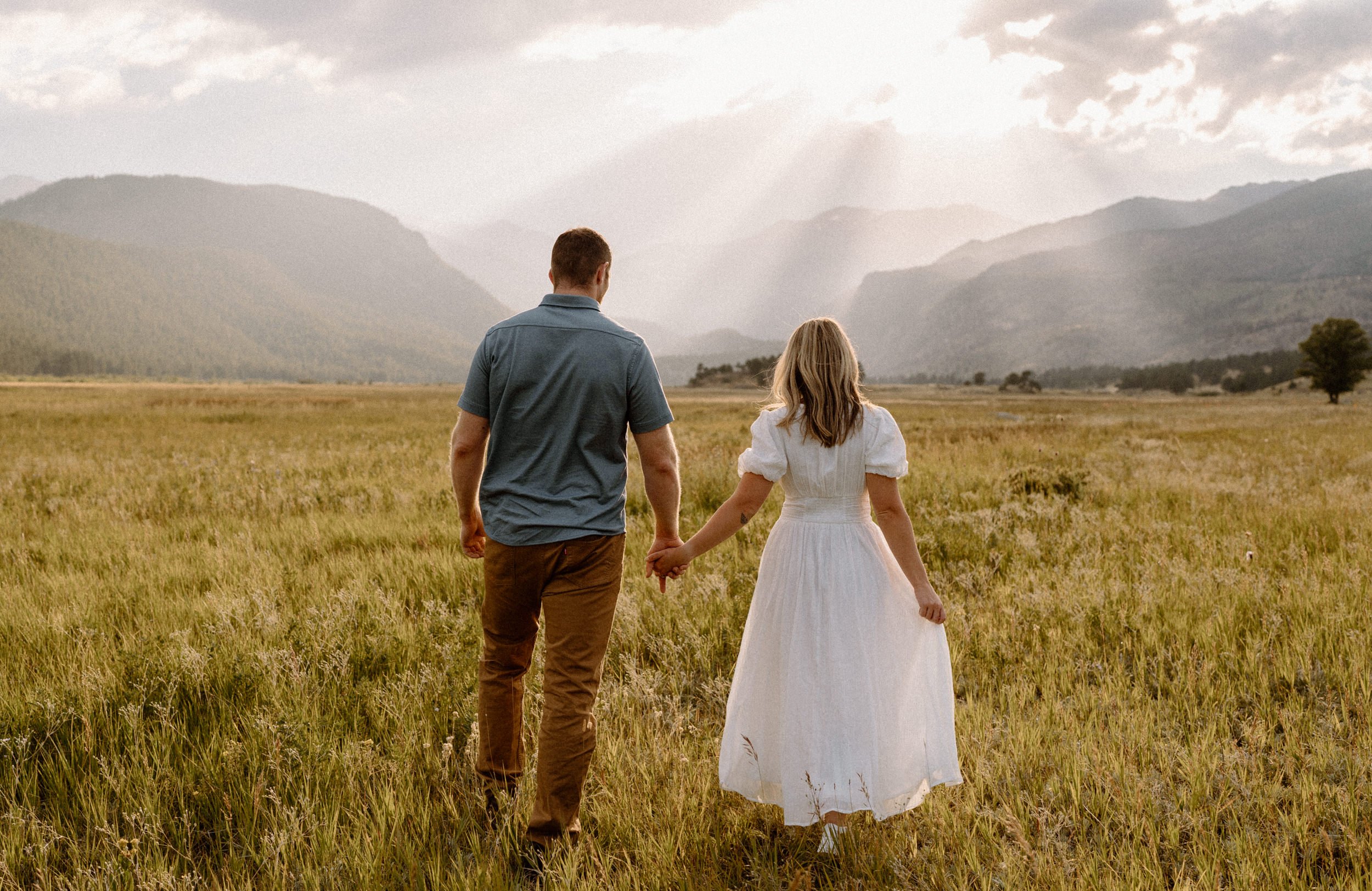 Man and woman hold hands walking through a meadow in Rocky Mountain National Park