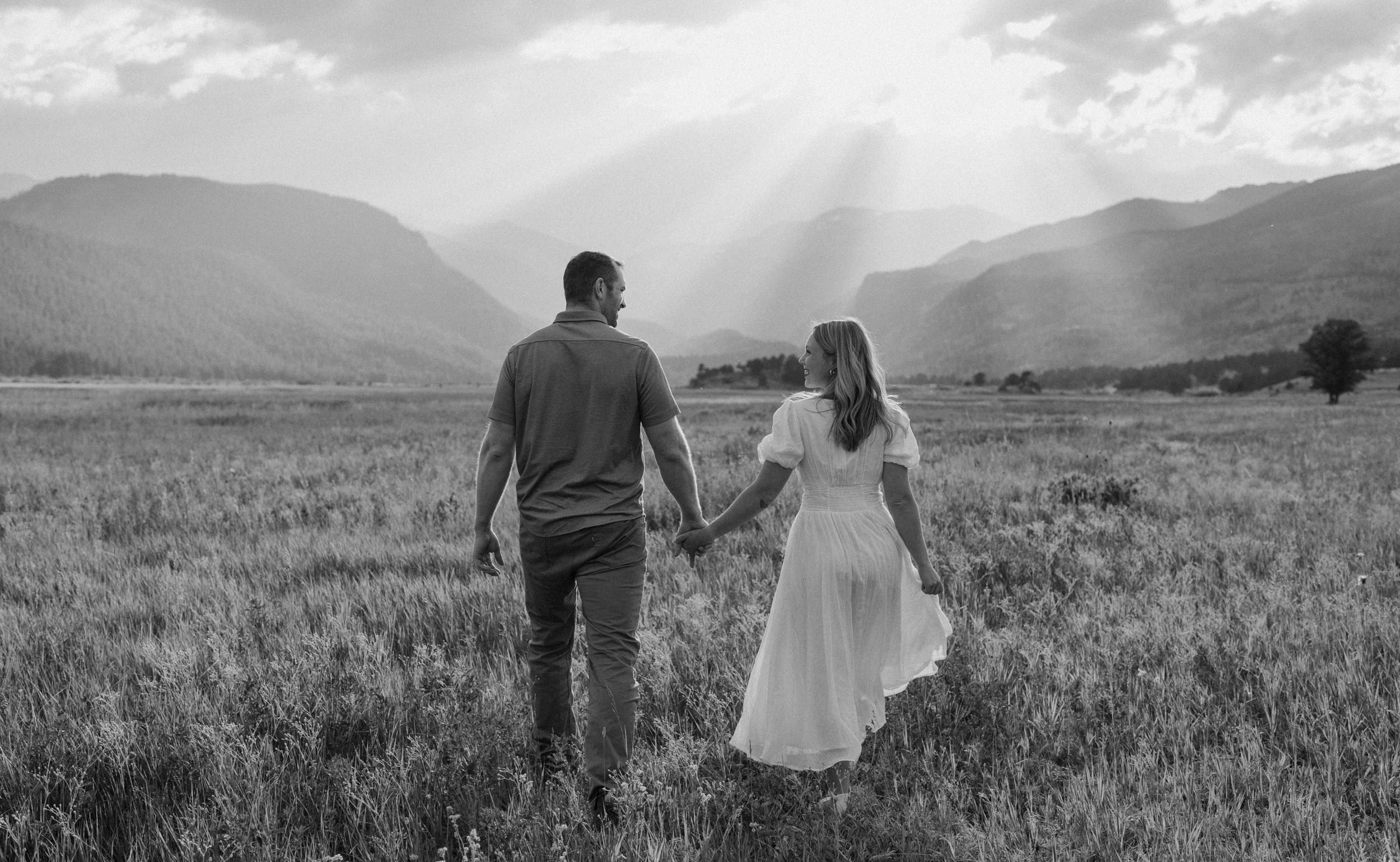 Man and woman hold hands in a meadow during engagement session in Rocky Mountain National Park