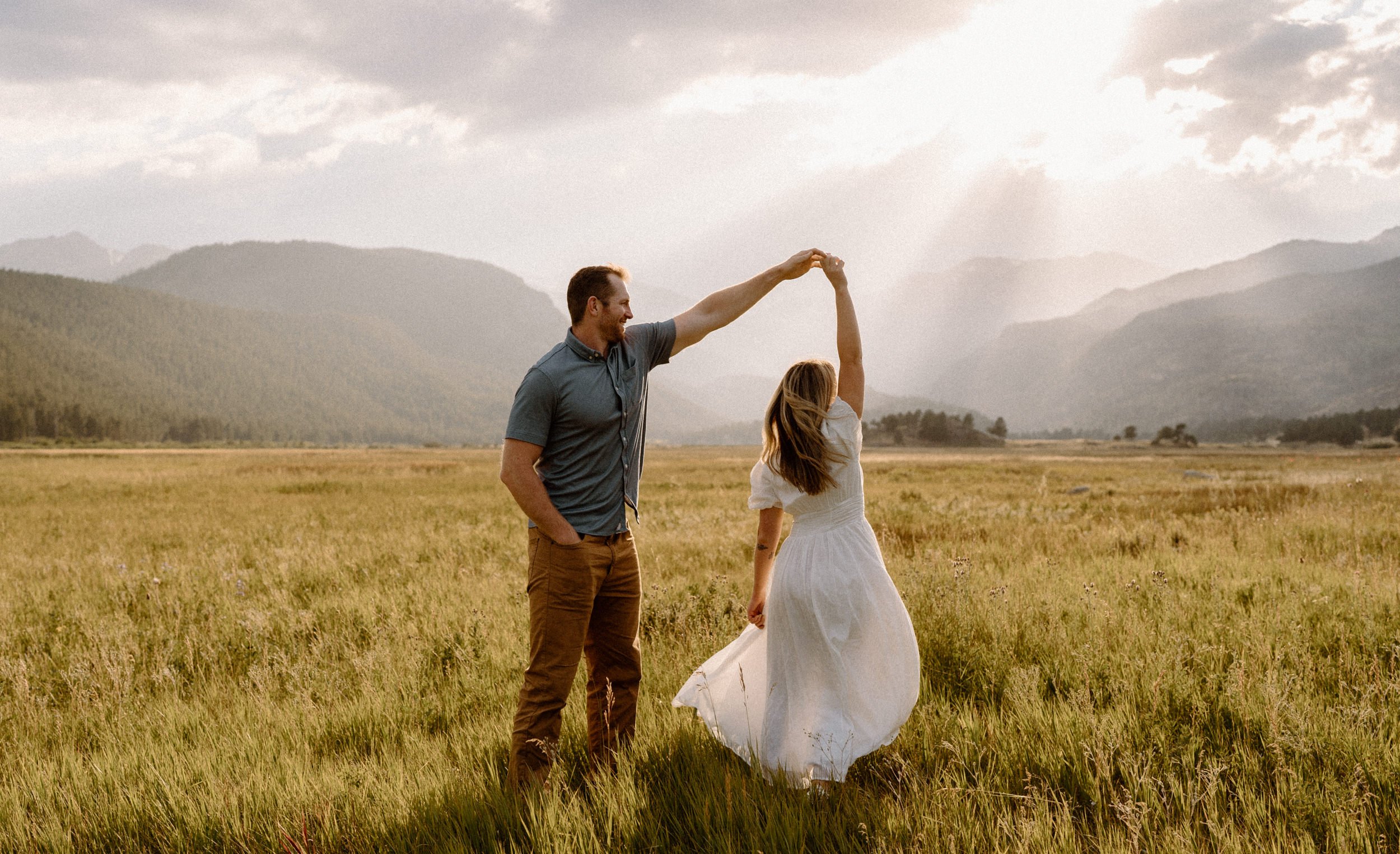 Man twirls woman in meadow during engagement session in Rocky Mountain National Park