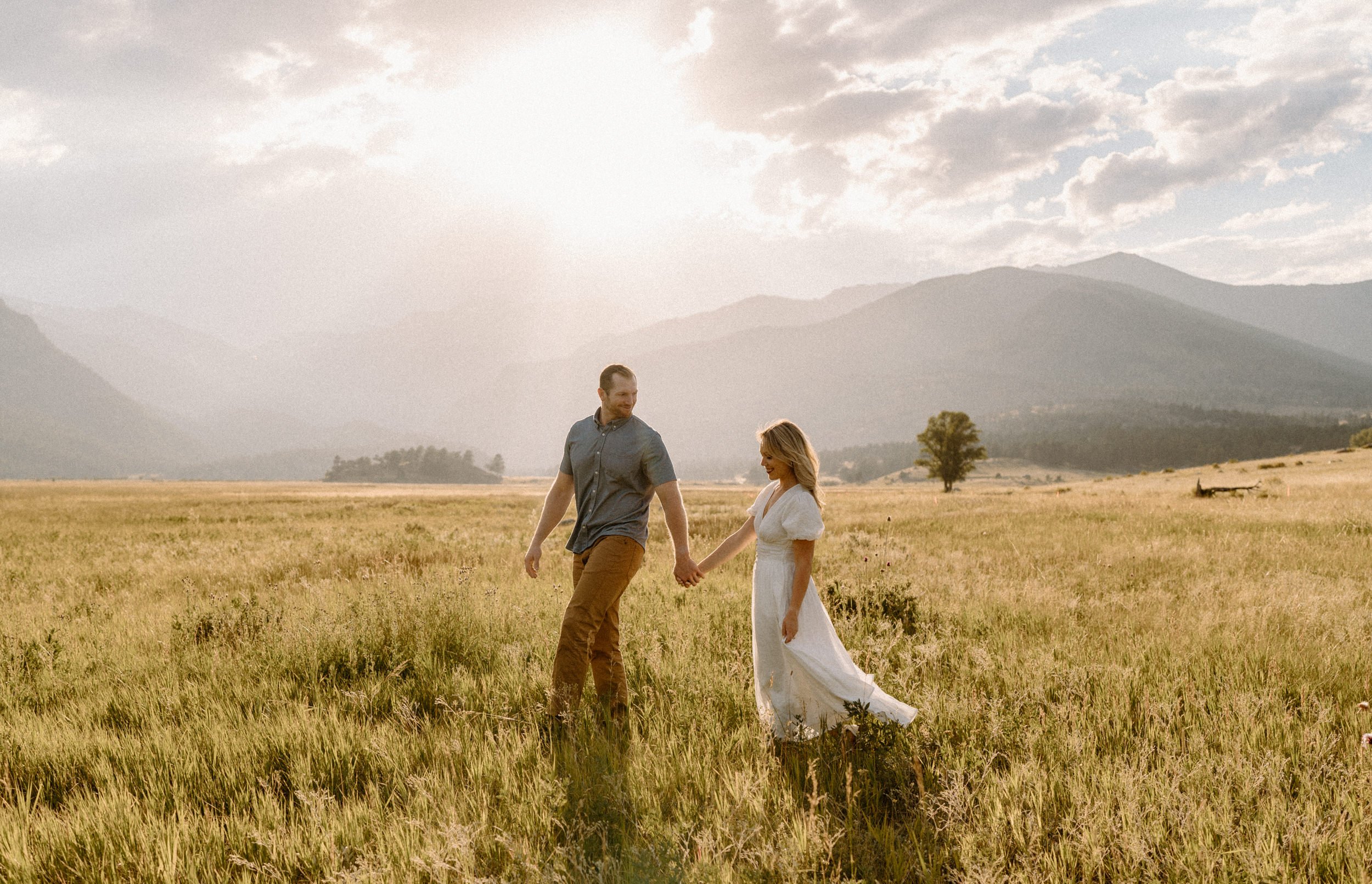 Man and woman hold hands while walking through a meadow in Rocky Mountain National Park
