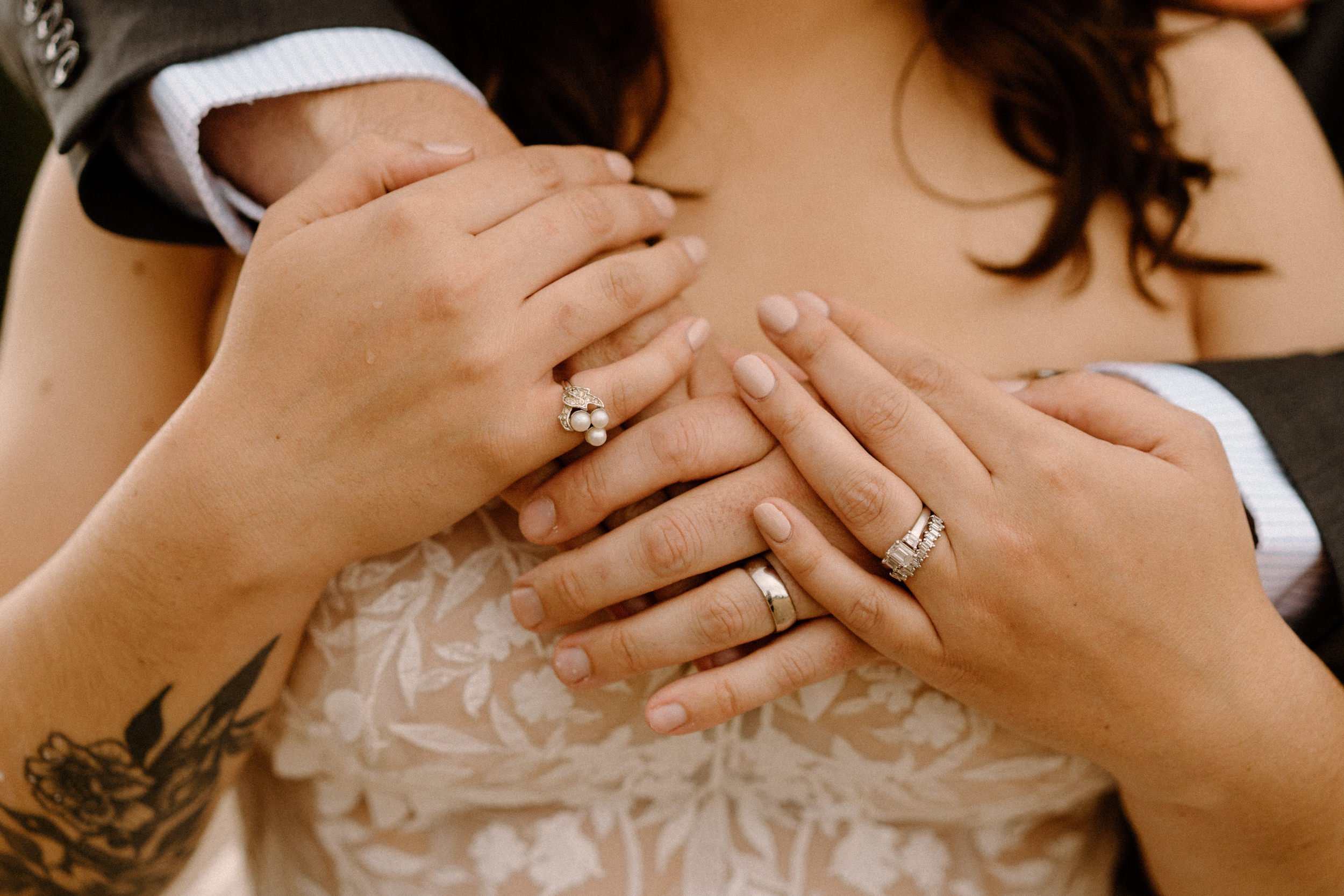 Groom hugs bride from behind, showcasing both of their wedding rings