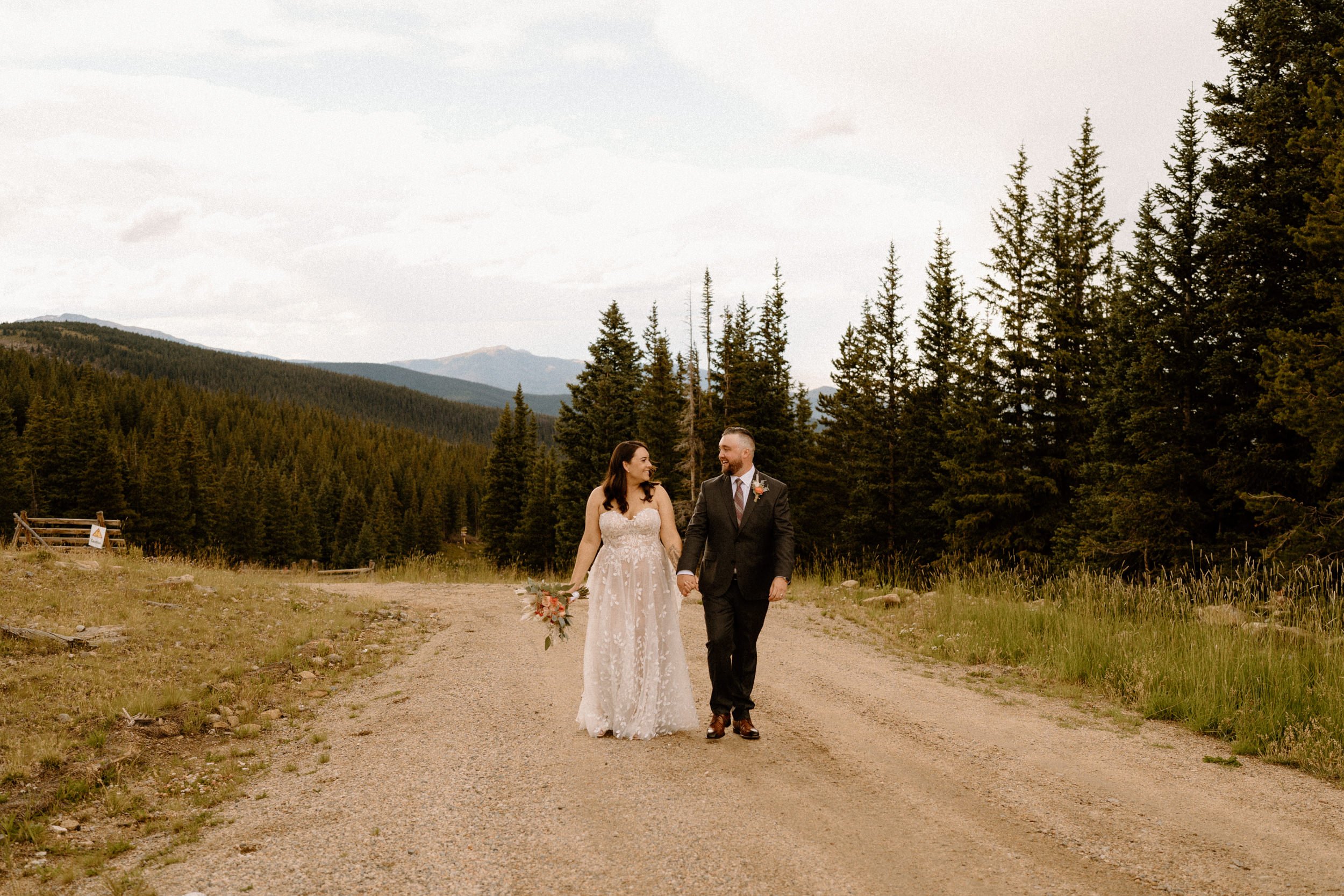 Bride and groom hold hands as they walk down a dirt road