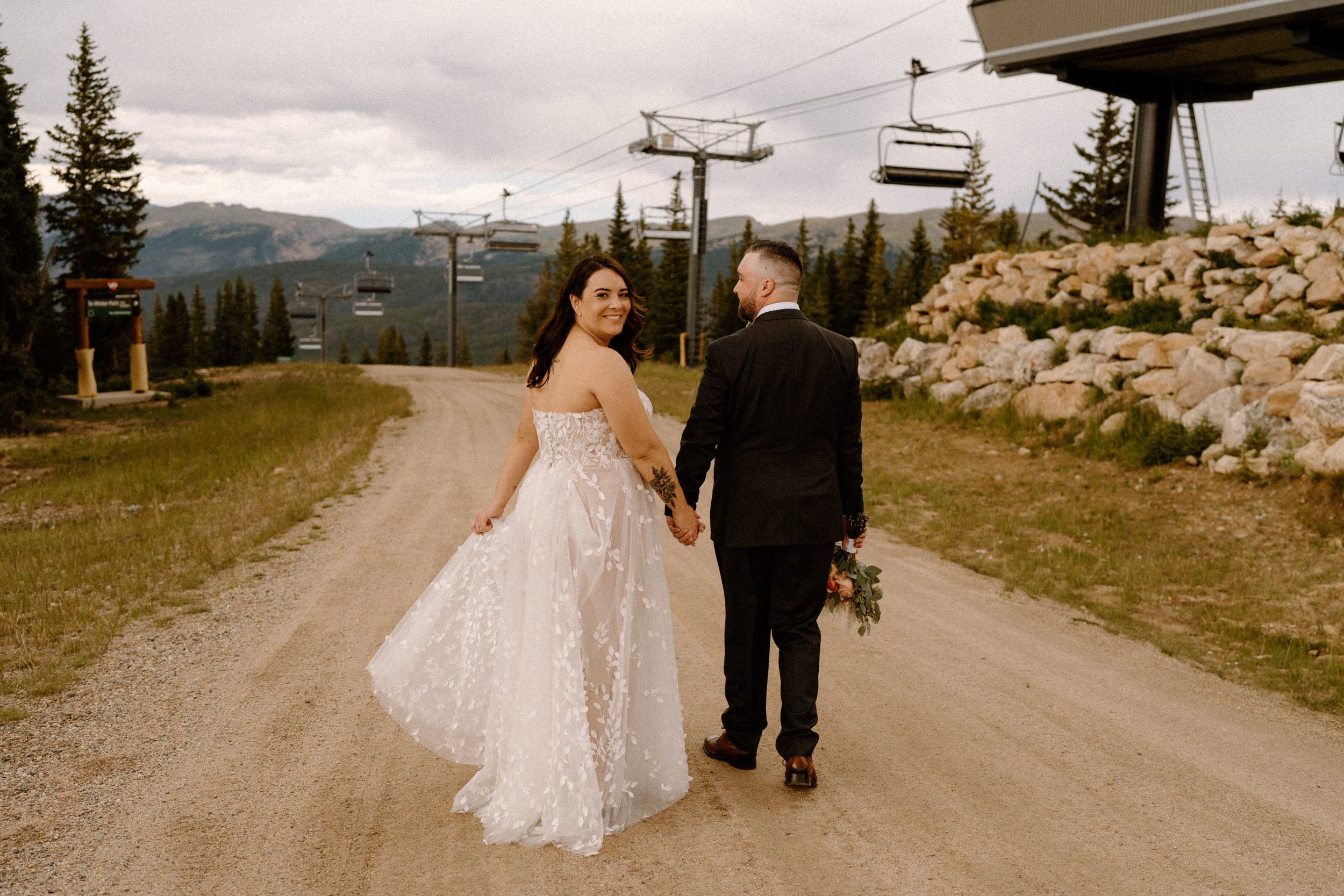 Bride and groom hold hands and walk toward the chairlift at Lunch Rock in Winter Park, CO