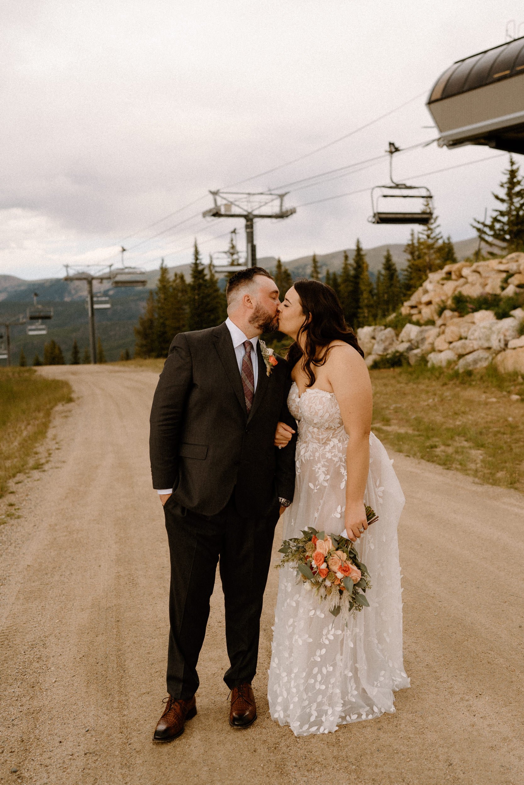 Bride and groom kiss in front of chairlifts at Lunch Rock in Winter Park, CO