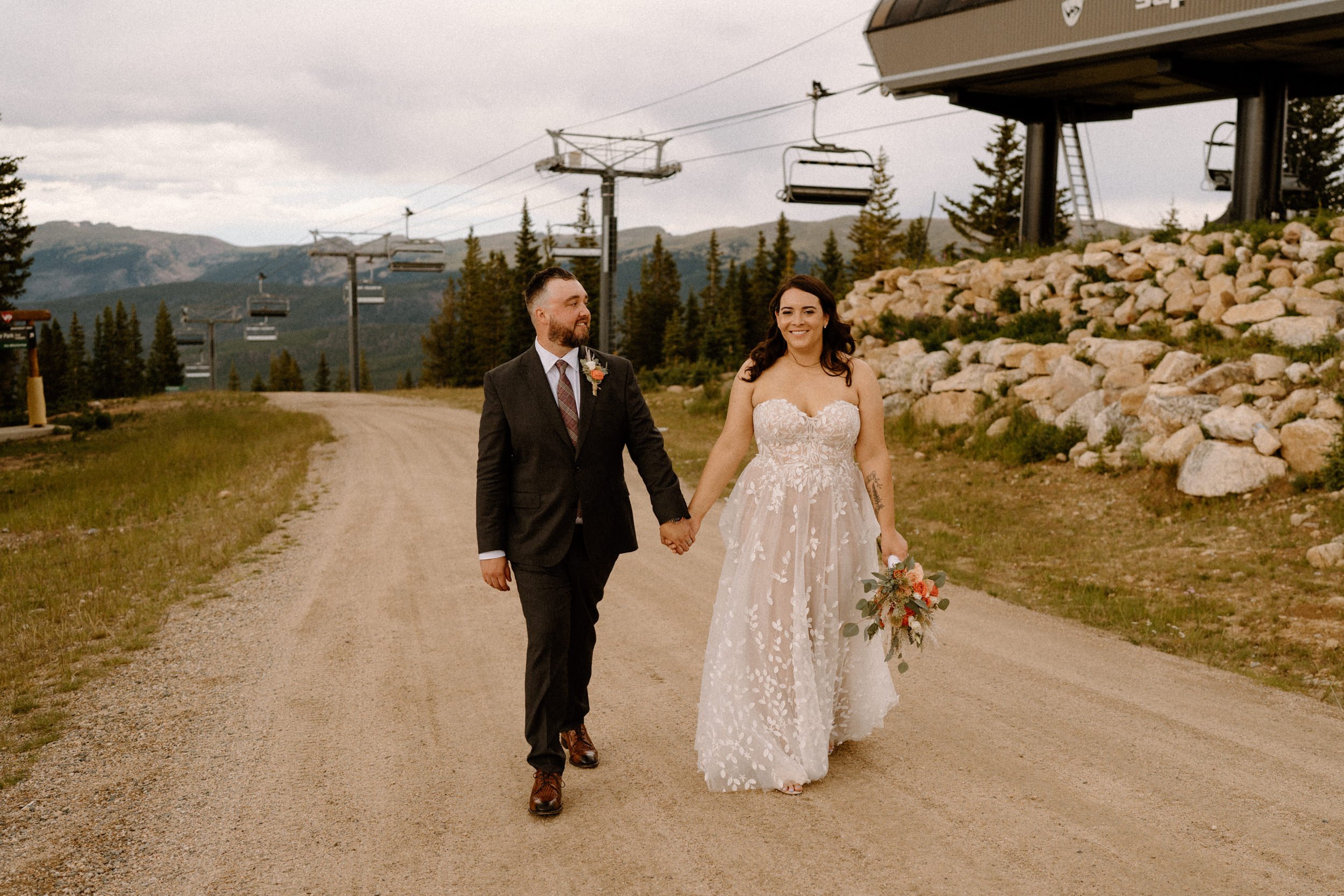 Bride and groom hold hands as they walk in front of the chairlift