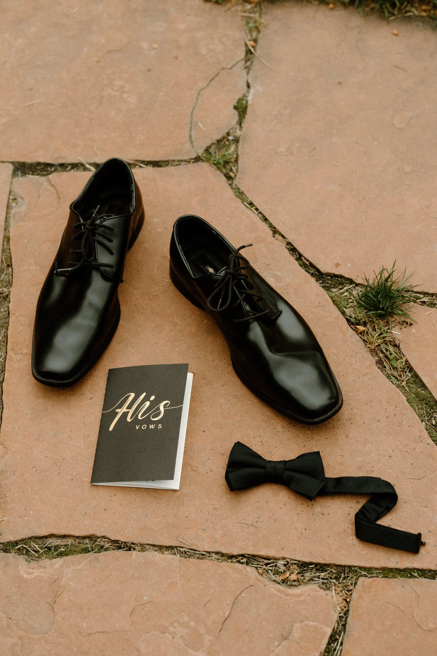 The groom's black shoes, his vow book, and a black bow tie