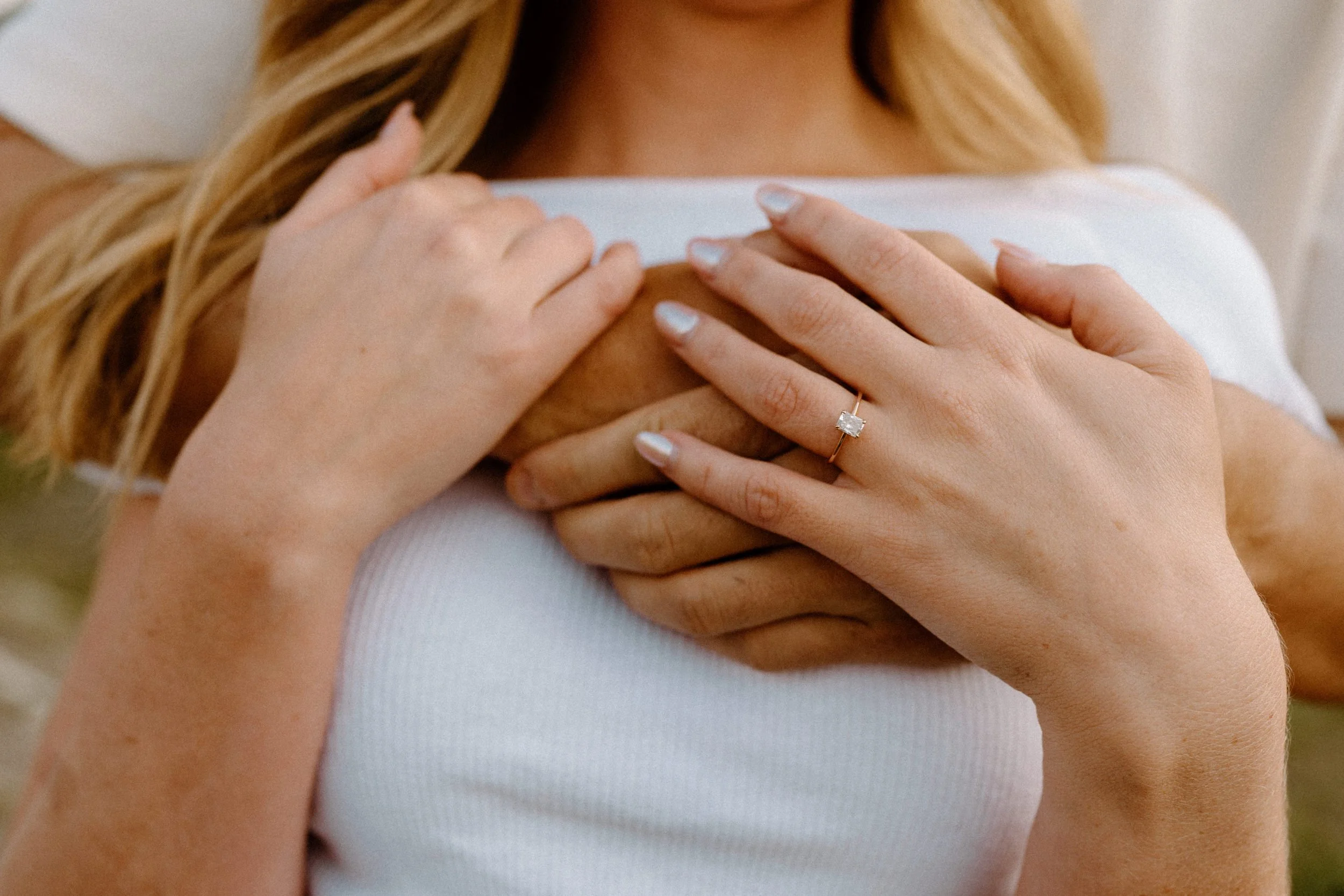 Fiancé hugging fiancée from behind showing engagement ring during engagement session at Loveland Pass