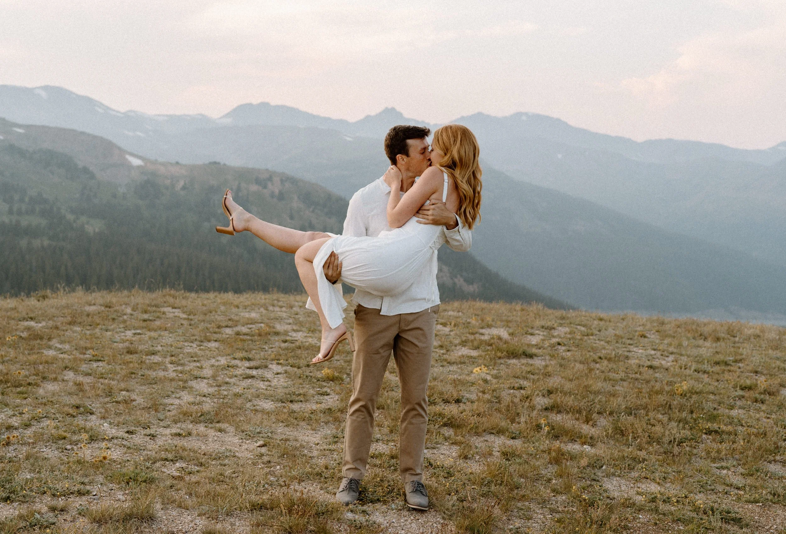 Fiancé holding fiancée and kissing her during an engagement session at Loveland Pass