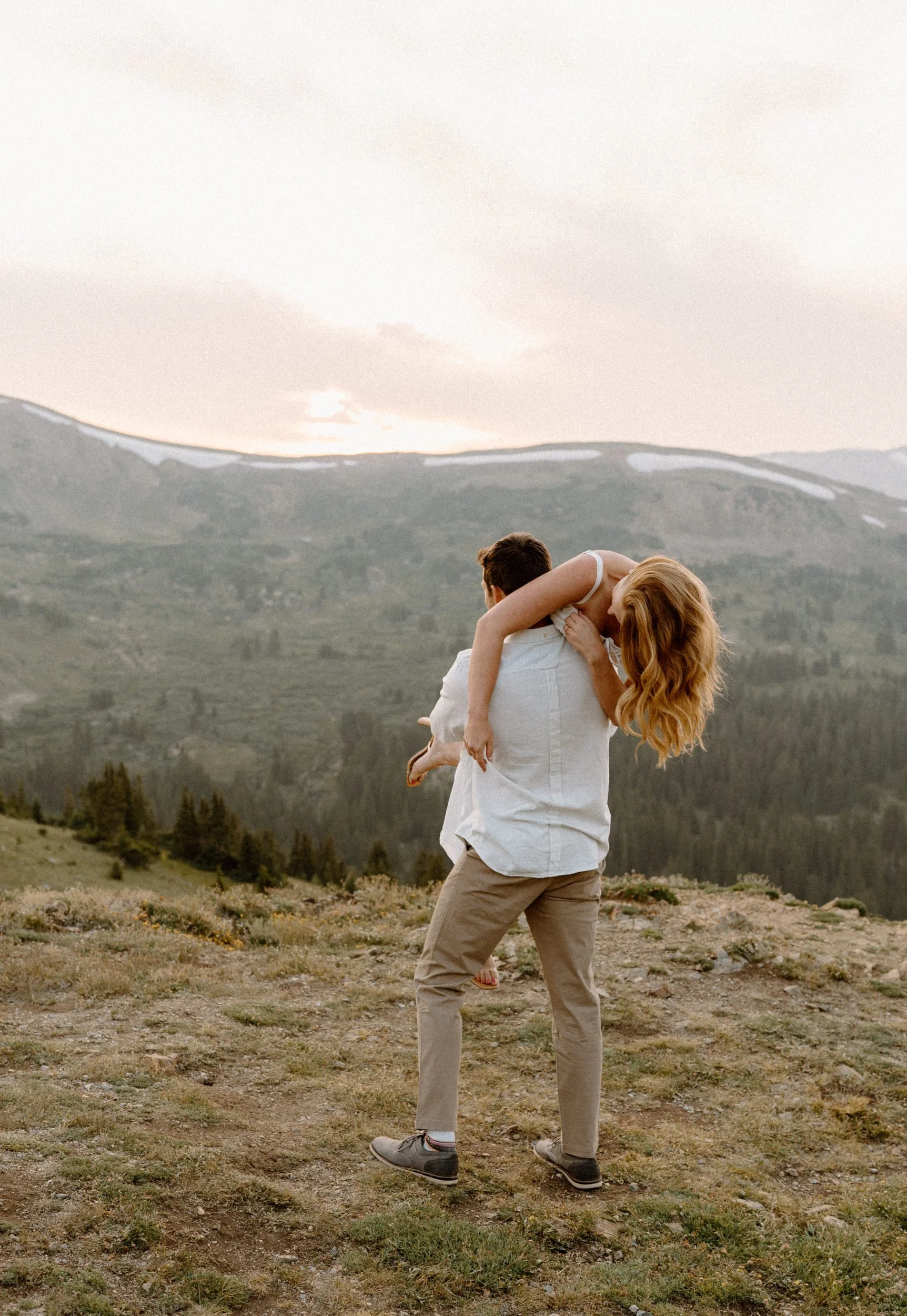 Fiancé carrying fiancée over his shoulder at Loveland Pass during an engagement photoshoot