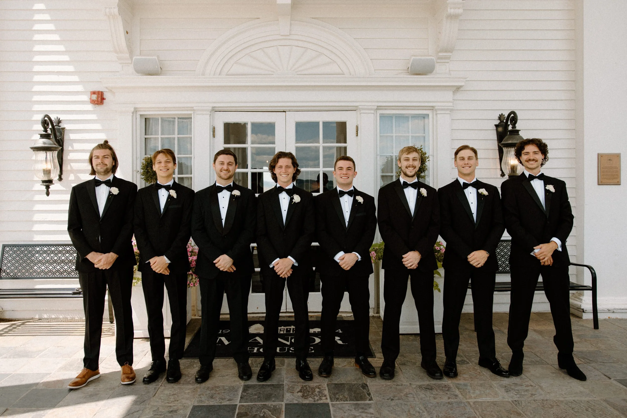 Groom and groomsmen smiling outside The Manor House on wedding day