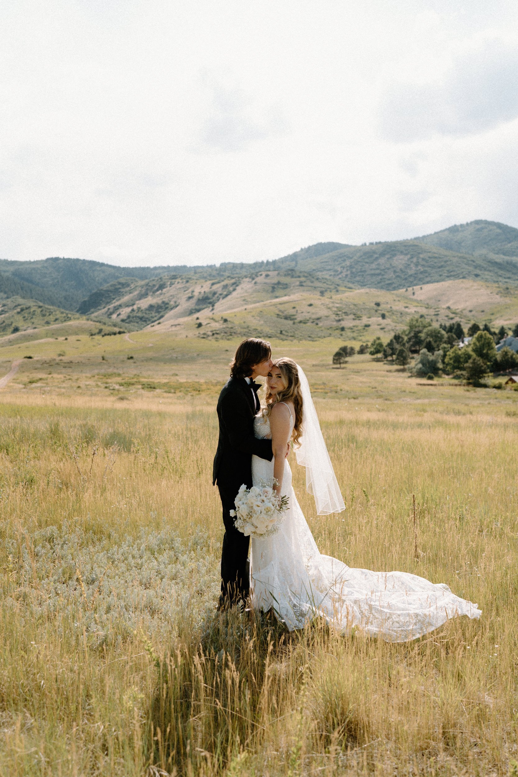 Groom kissing bride's forehead in a field on wedding day at The Manor House