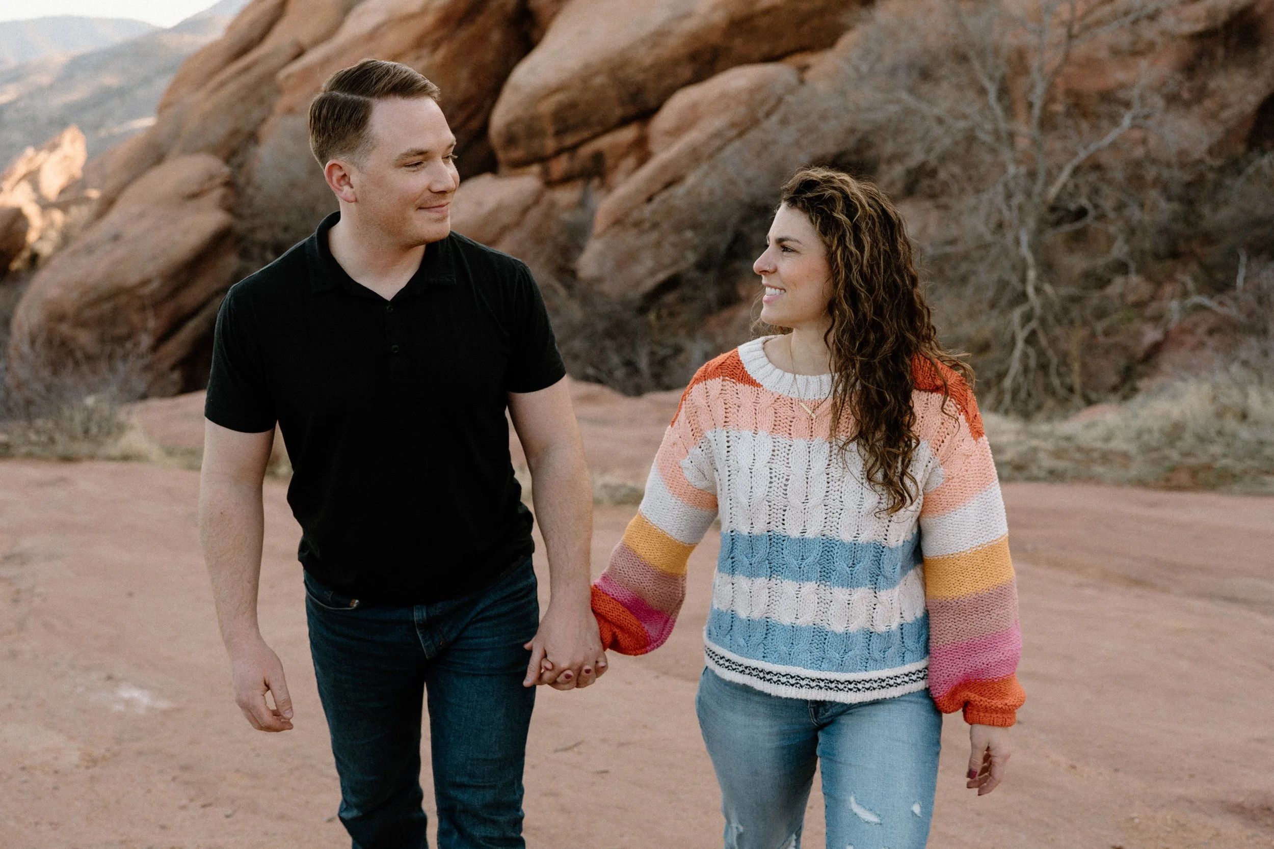 Couple holding hands and walking in Red Rocks during engagement session