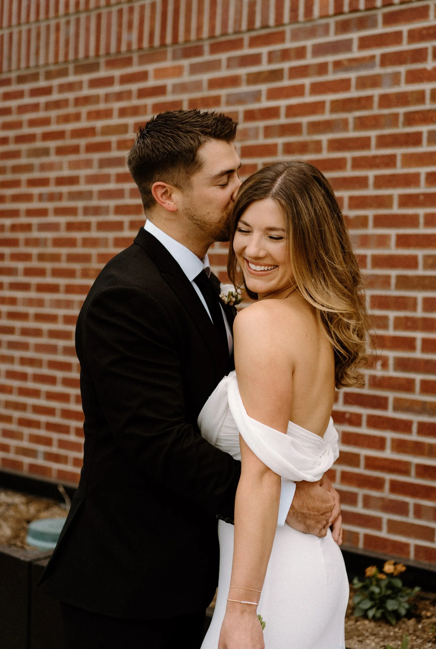 Bride smiling while groom kisses her forehead on wedding day at The Eddy in Golden Colorado