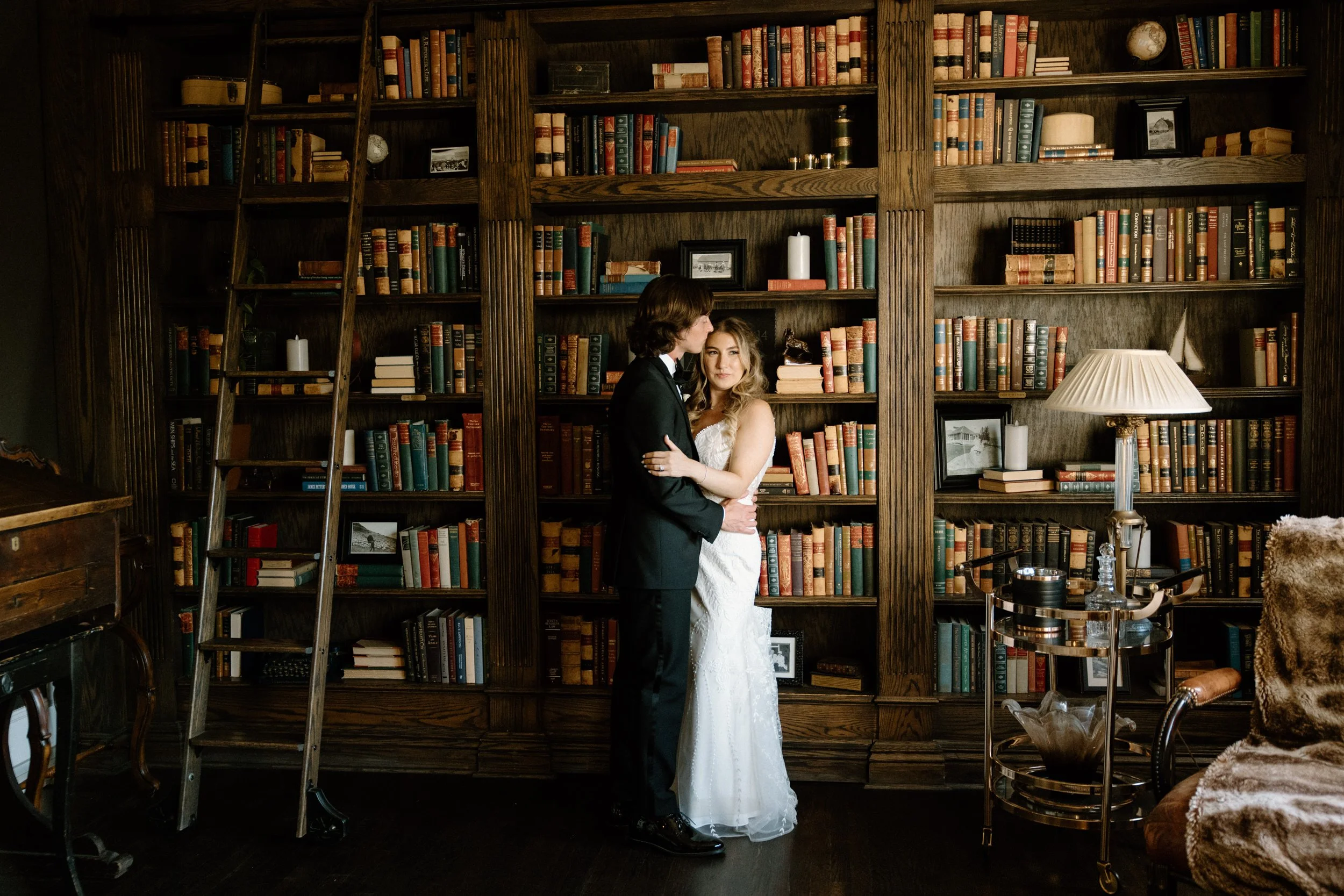 Groom kissing bride's forehead in the library at The Manor House