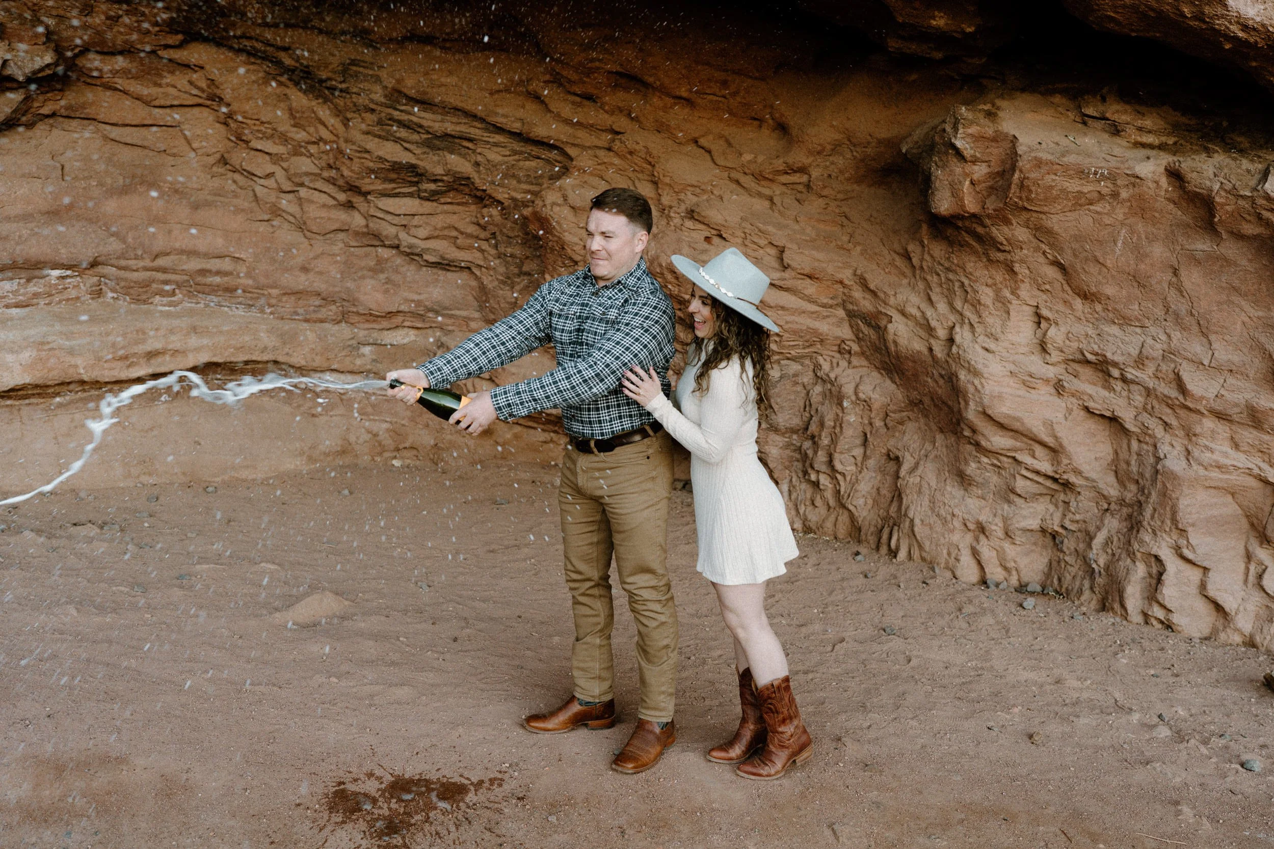 Fiancé popping champagne bottle during engagement session at Red Rocks