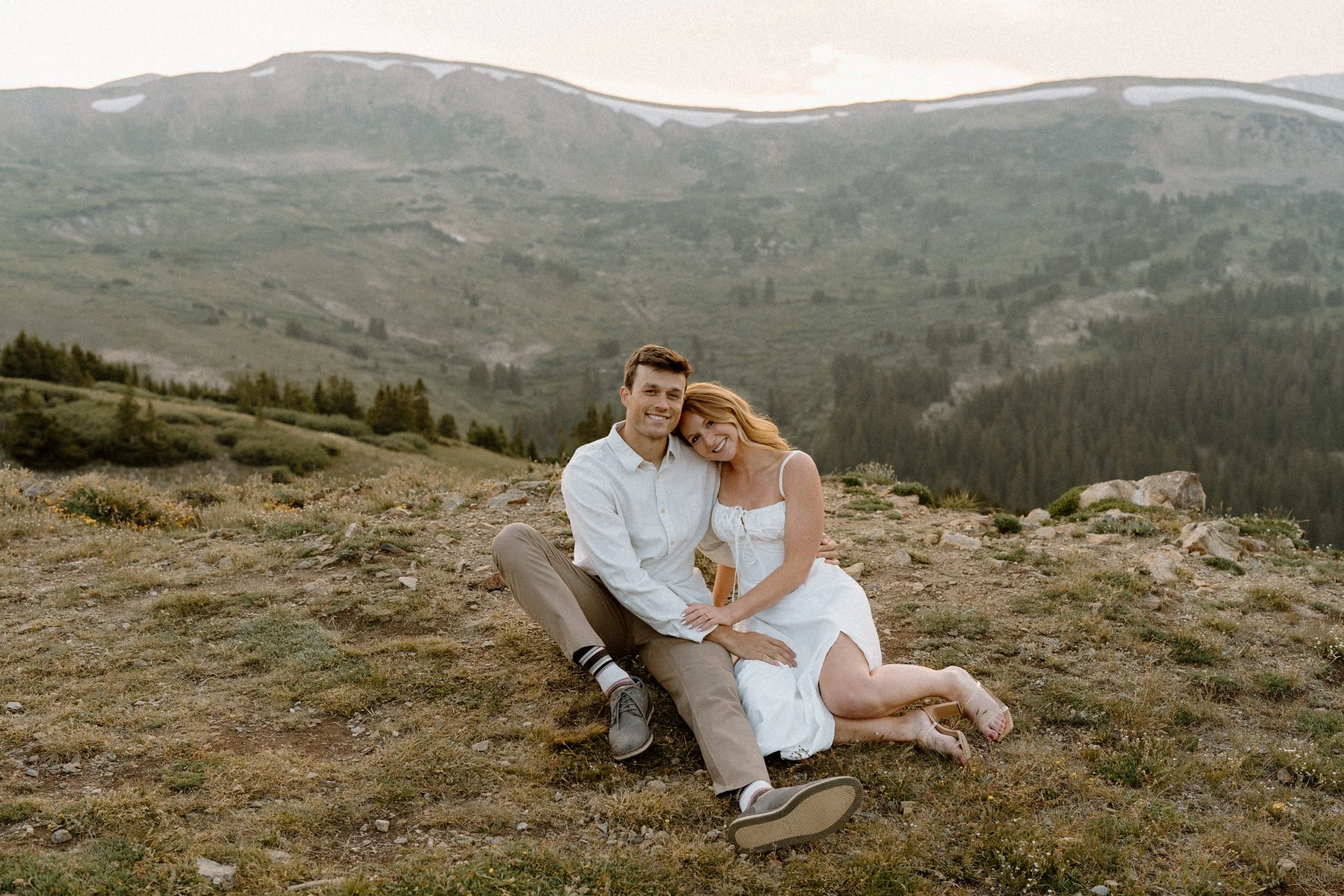 Couple sitting in a field at Loveland Pass and smiling during engagement session