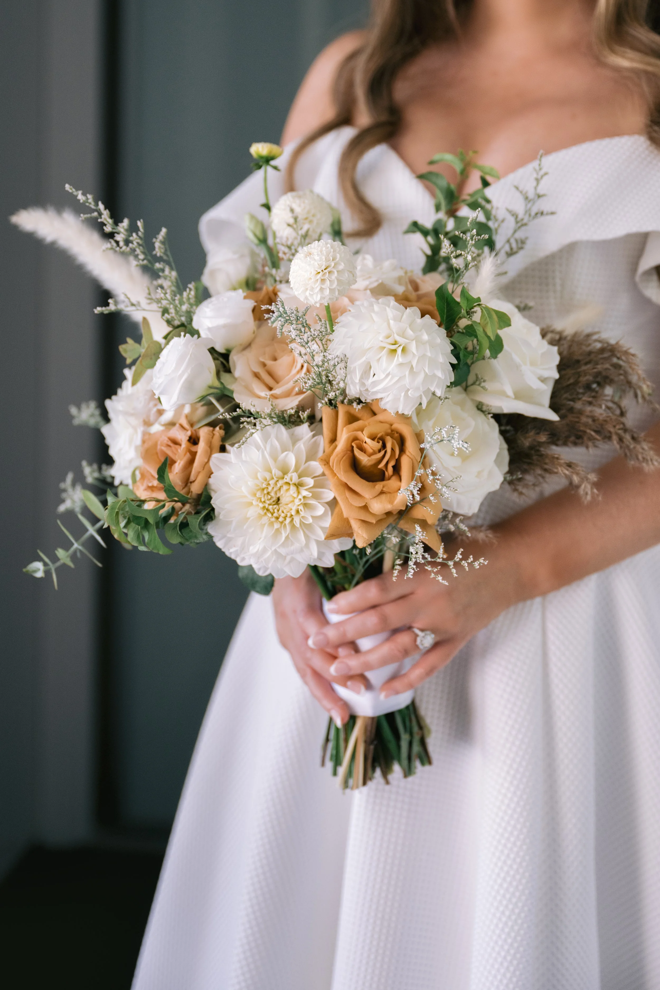 A woman in a white dress holding a bouquet of white and peach flowers with greenery, standing indoors.