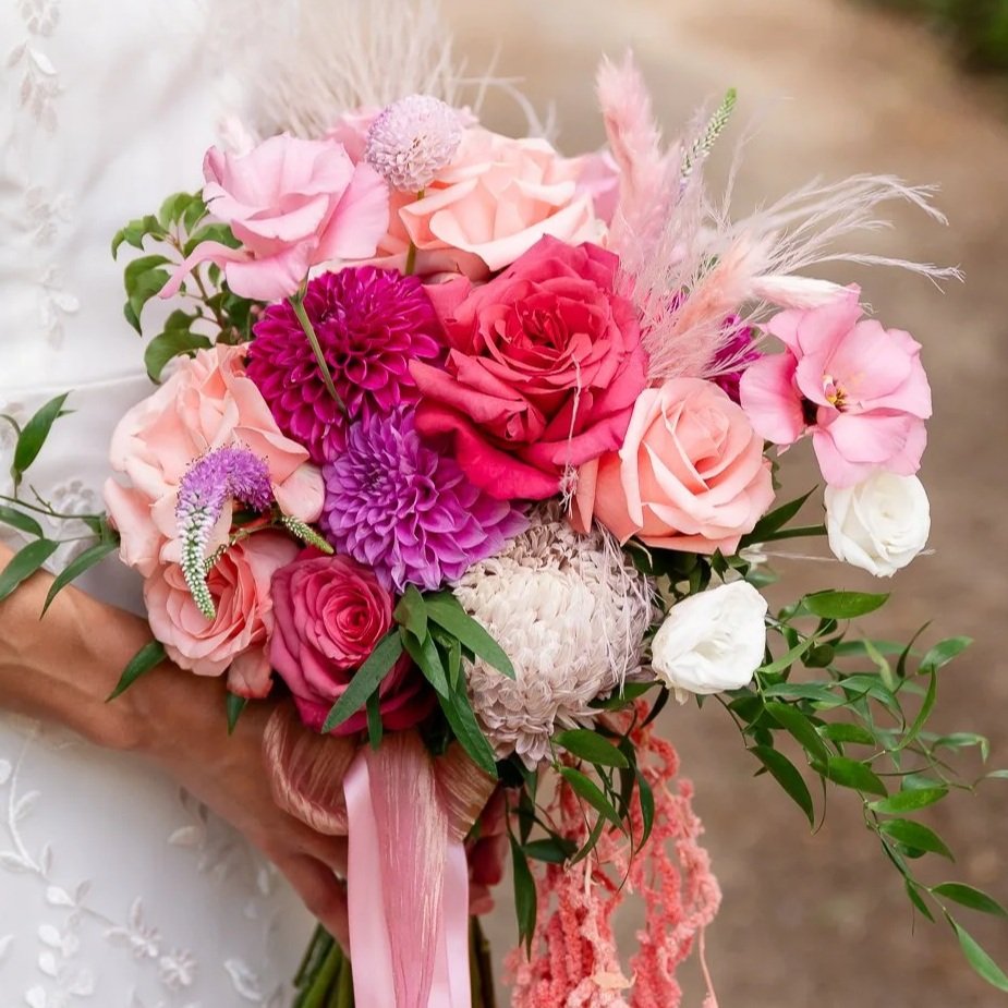 A colorful bouquet of pink, purple, and white flowers held by a person in a wedding dress.