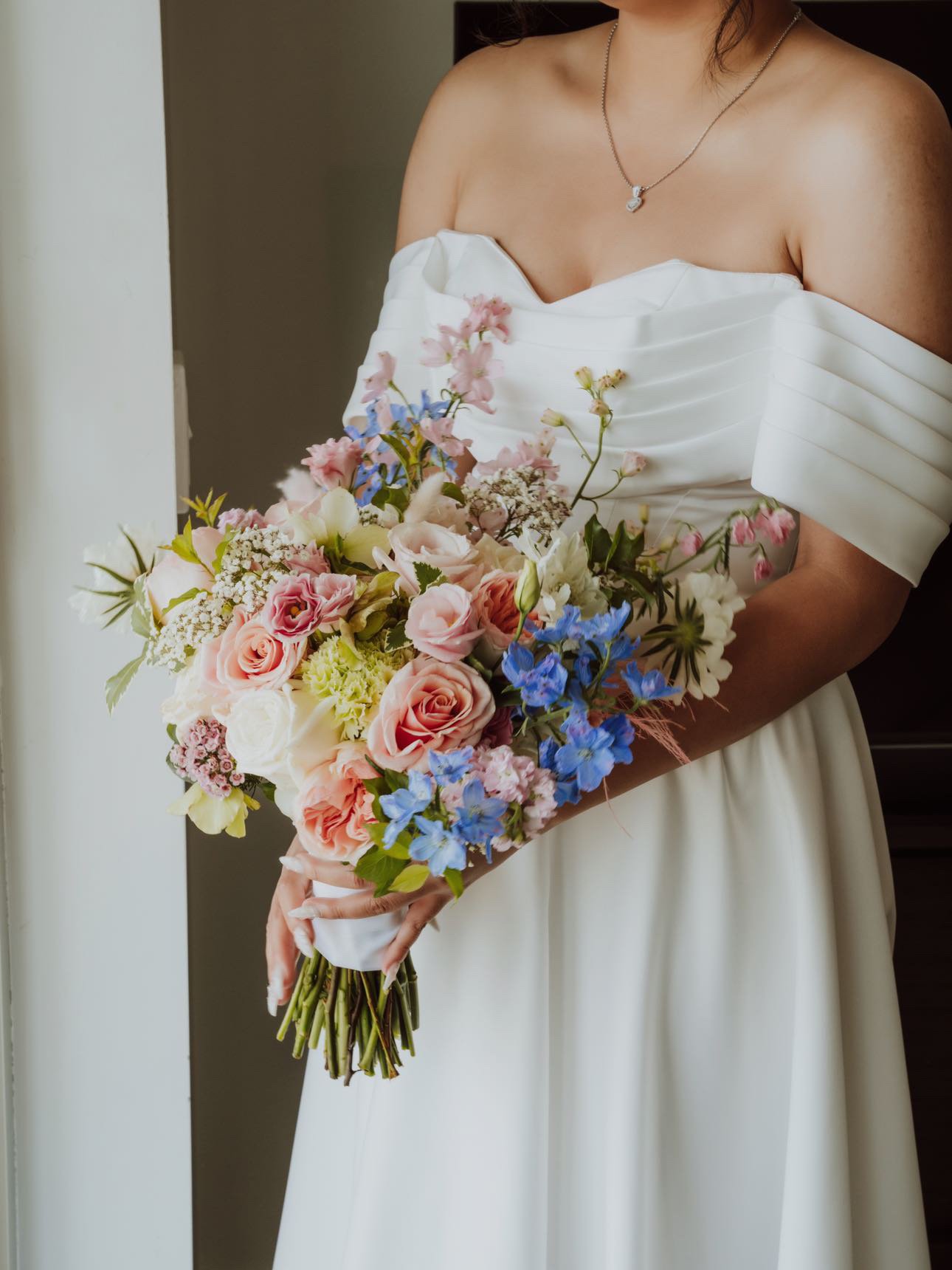 A woman in a white off-shoulder dress holding a colorful bouquet of flowers.