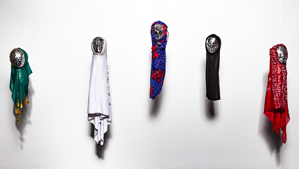 Title: Let’s Face It Year: 2017- Ongoing Medium: Installation including fabric, Styrofoam, ink, fishing line Dimensions: each sculpture is 6 inches x 30 inches Description:Five mixed media sculptures wrapped in hijabs featuring different fabric manipulations including screen print, paint, and embroidery. Viewers are encouraged to interact by leaving their interpretation on note cards