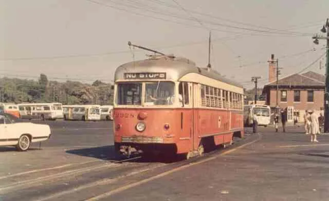 Trolley # 3328 waits for its next trip at the Arborway yard in this 1968 photo. Idle buses can be seen along with passenger waiting to board near the MBTA business office.