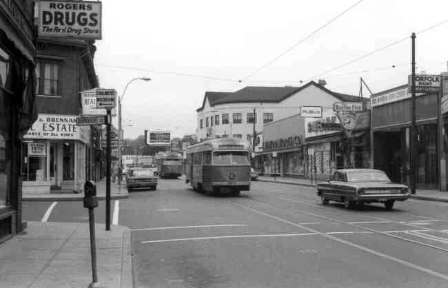 Two trolleys approach Centre & Burroughs Streets in this 1969 photo. Rogers Drugs, O'Leary & Brennan Real Estate, Yumont Hardware, Publix Market, Boston Five Cents Savings Bank, and F. W. Woolworth were a few of the businesses at the time. 