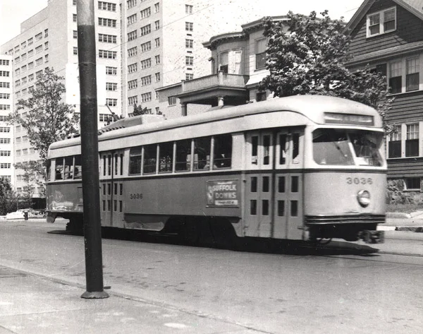 A green line trolley heads out South Huntington Ave. having just passed the VA Hospital. October 29, 1956. An ad for Suffolk Downs appears on the side of the car.
