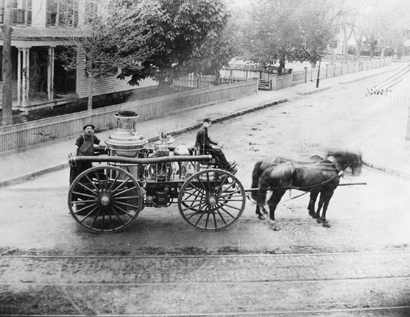Two firemen pose with a horse-drawn chemical fire engine in this 1880 photograph taken at Centre and Burroughs Streets. These engines used chemicals rather than water to fight fires.
