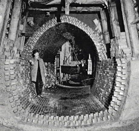 High level sewer construction in sand at Forest Hills, Jamaica Plain. Note bin suspended from overhead crane with trolley used to remove excavated dirt from tunnel. Due to the sandy nature of the soil in this area, wooden beams resting on a foundation provide support for the roadway above. From Metropolitan Water and Sewage Board First Annual Report. January 1, 1902. 