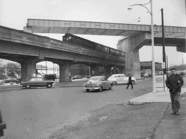 As a train travels towards downtown Boston along the Boston Elevated Railway at Forest Hills, a portion of the new Monsignor William J. Casey Overpass (Morton St.) is being constructed above.