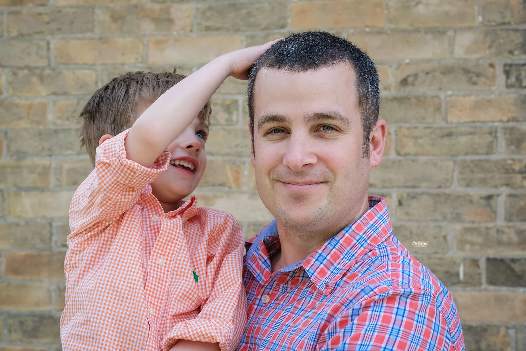 Boy ruffling Dad's hair outside in front of a brick wall Family photography Kitchener-Waterloo