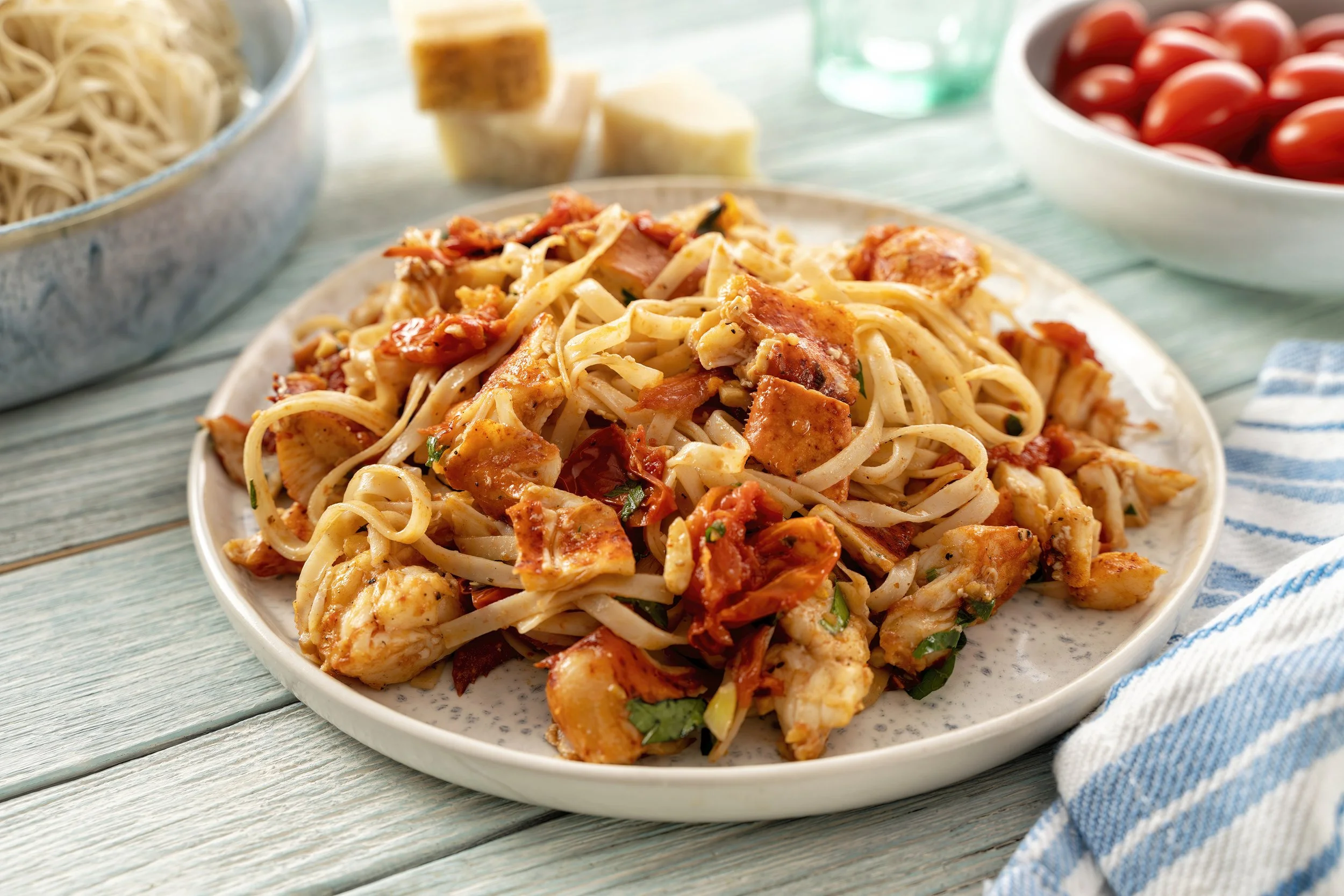 Plate of pasta with tomato sauce, chicken pieces, and herbs, on a wooden table with a blue and white dish towel.