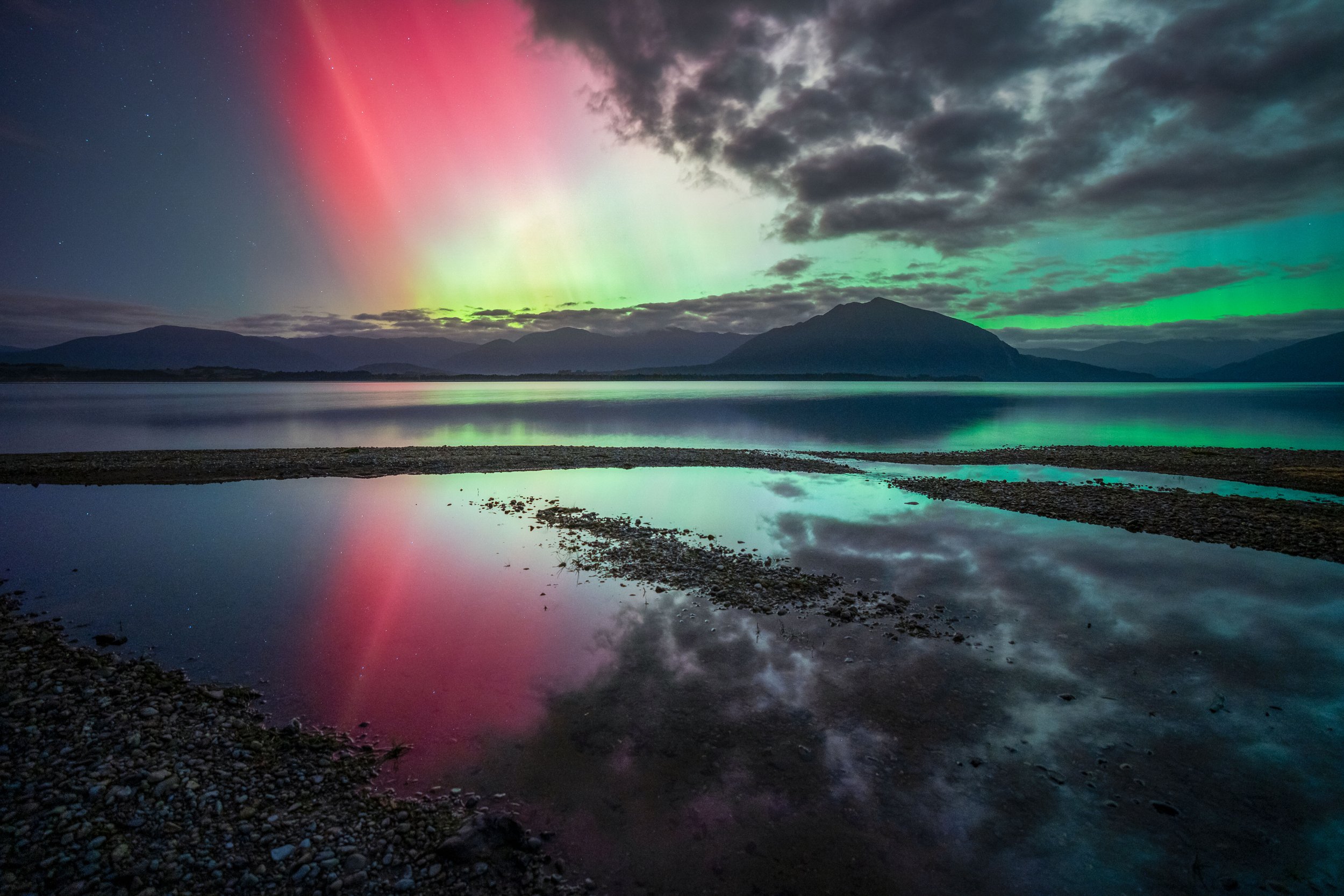 Lake Brunner in New Zealand under the aurora australis, showing colorful northern lights reflected in the lake