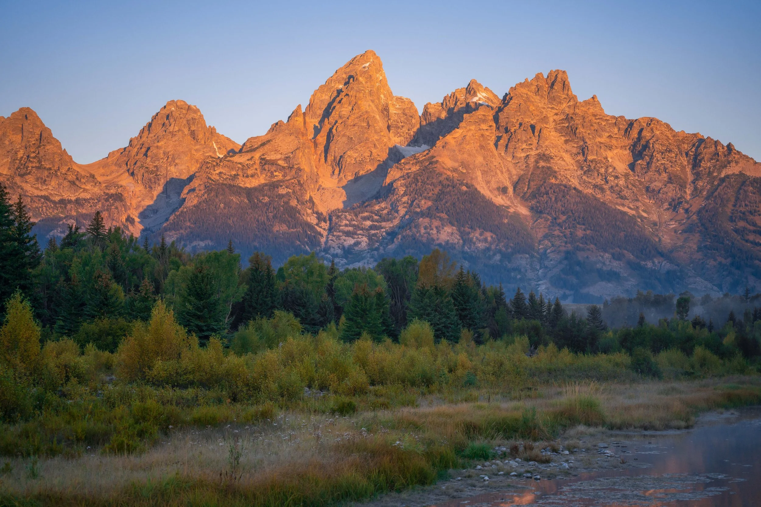 Grand Teton mountain range at sunrise in Wyoming, USA, showing jagged peaks, valleys, and colorful sky reflected on alpine terrain