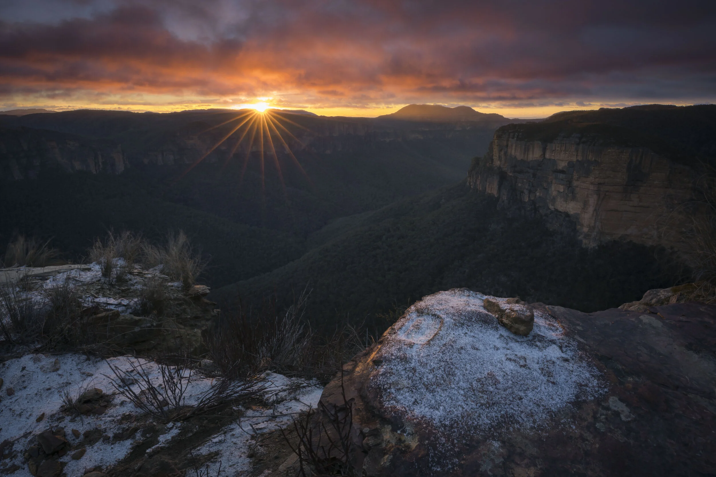 Snow-covered cliffs and valleys of the Blue Mountains illuminated by a vibrant sunrise with colorful sky