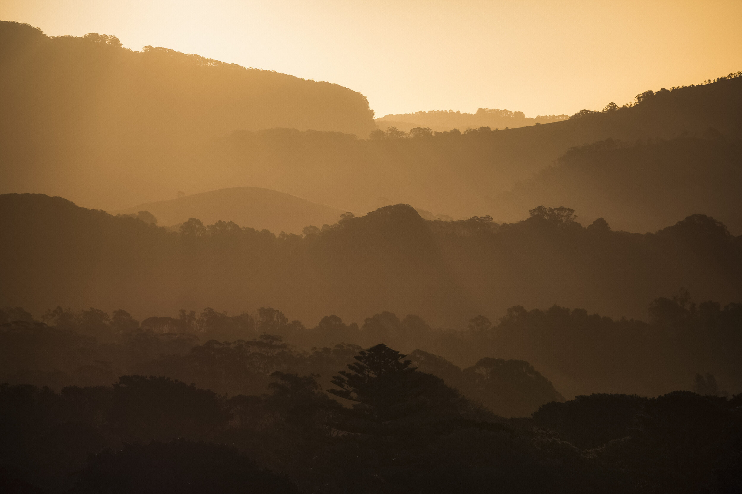 Rolling hills layered into the distance under a vibrant sunset sky, with warm light illuminating the contours of the landscape