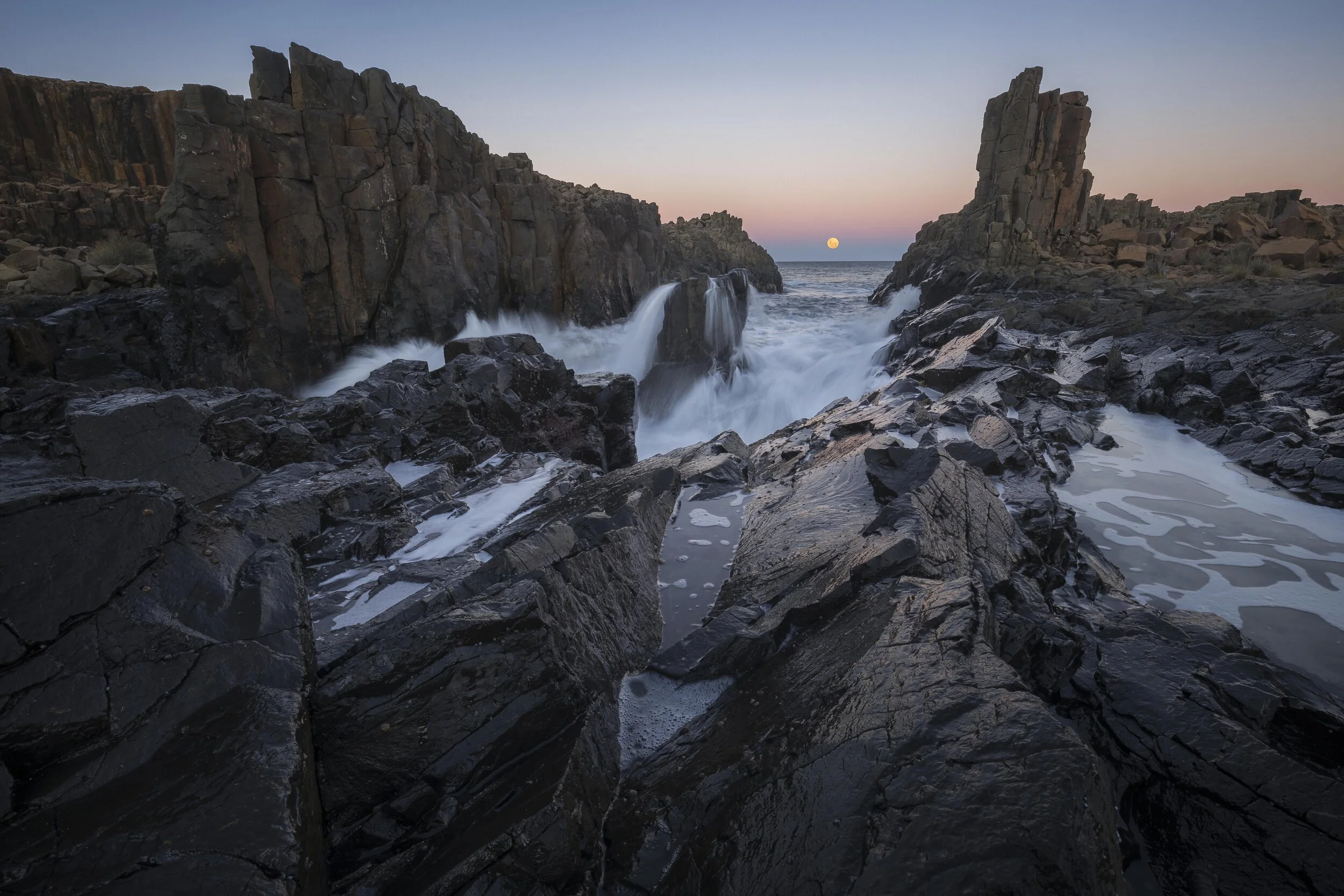 Full moon rising over Bombo Quarry with reflections on wet rocks