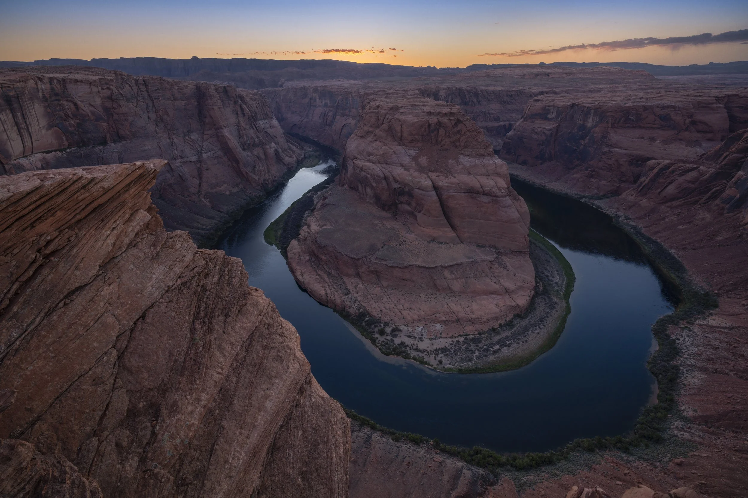 Horseshoe Bend in Arizona at sunset, showing the Colorado River winding around dramatic red rock cliffs under a colorful sky