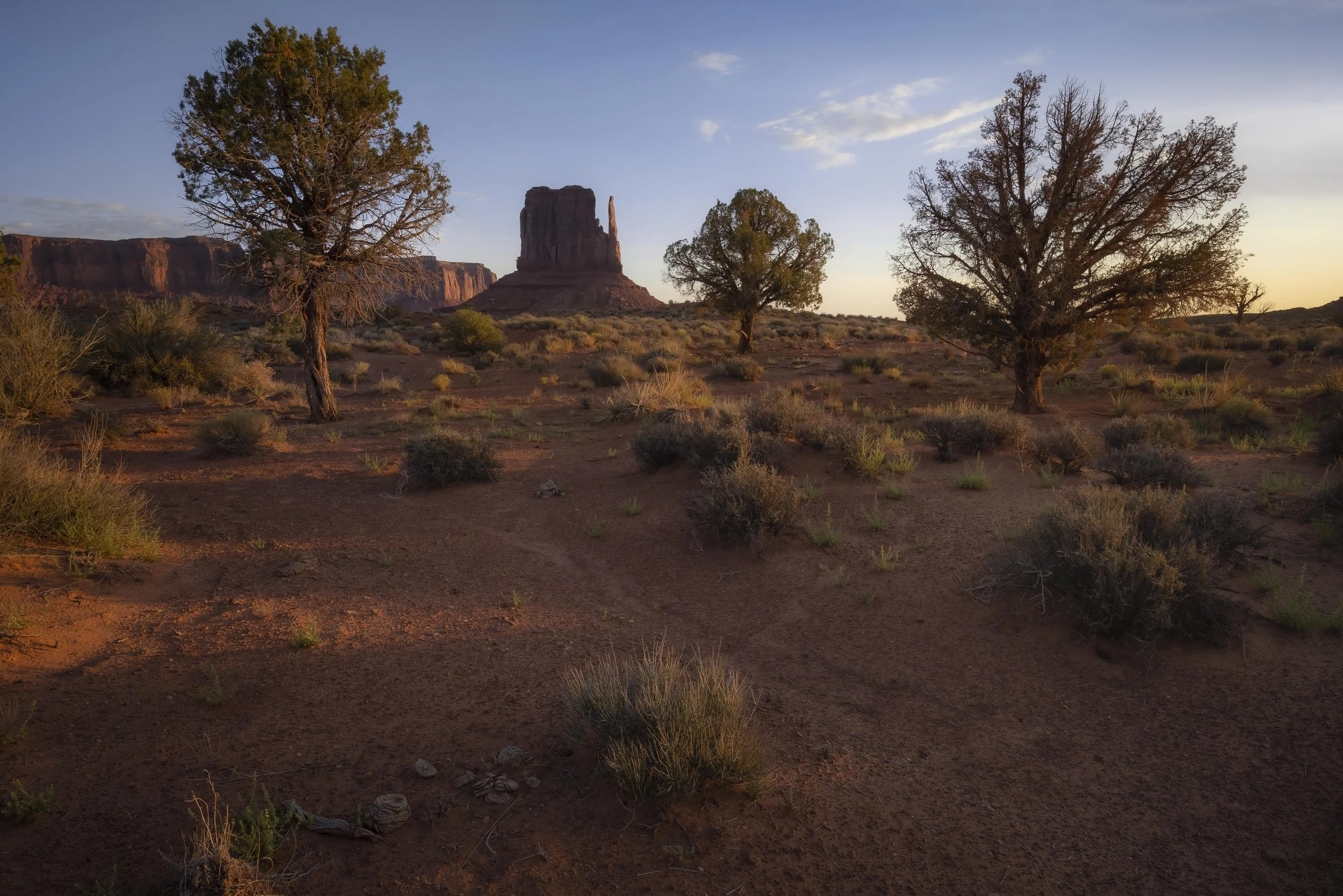 Monument Valley at sunrise, showing red sandstone formations, desert terrain, and soft golden light across the landscape