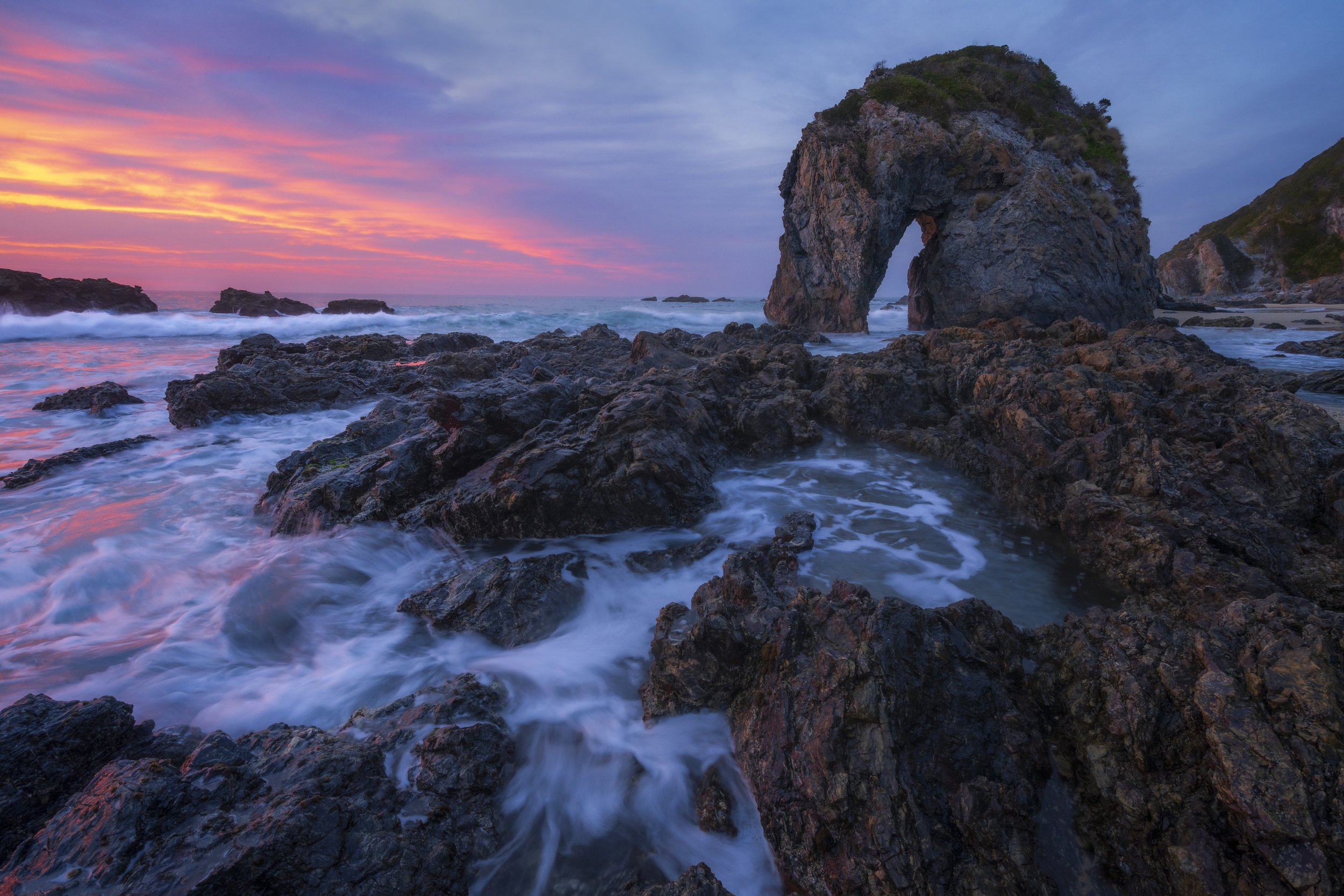 Colourful sunrise sky above Horse Head Rock with waves along the coast