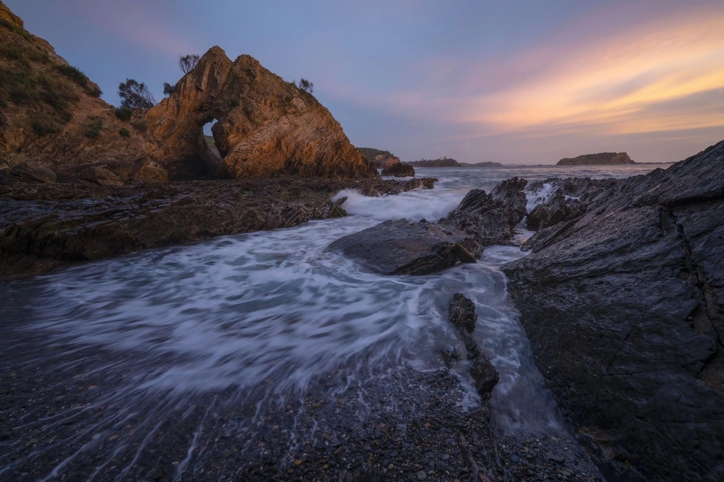 Coastal rock arch in Eurobodalla with ocean waves and sunrise sky