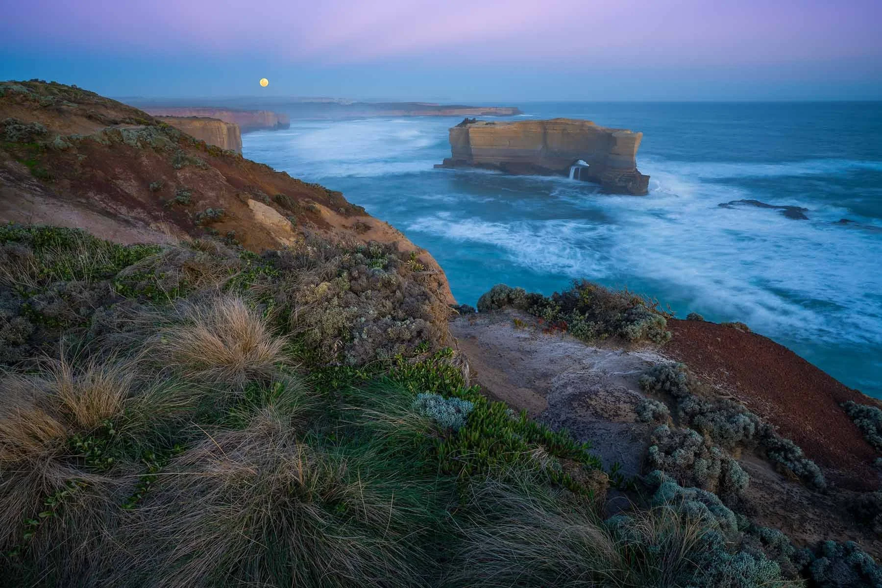 The full moon rises in the distance over the bakers oven on the Great Ocean Road, Victoria, Australia